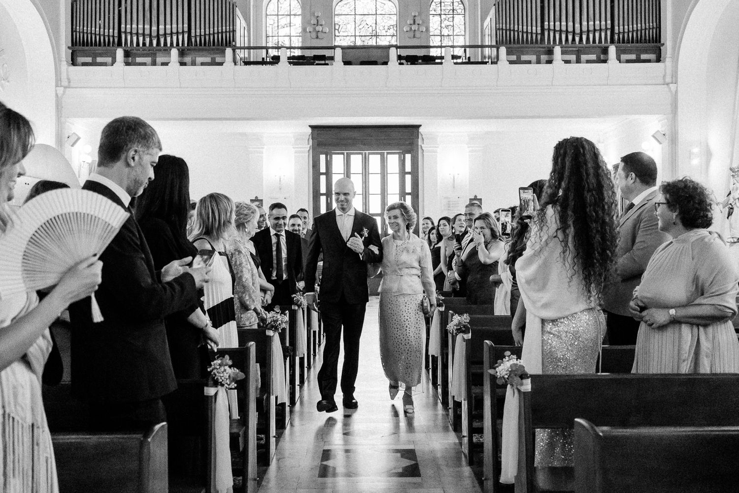 Black and white photo of a bride and groom walking down the church aisle surrounded by smiling wedding guests.