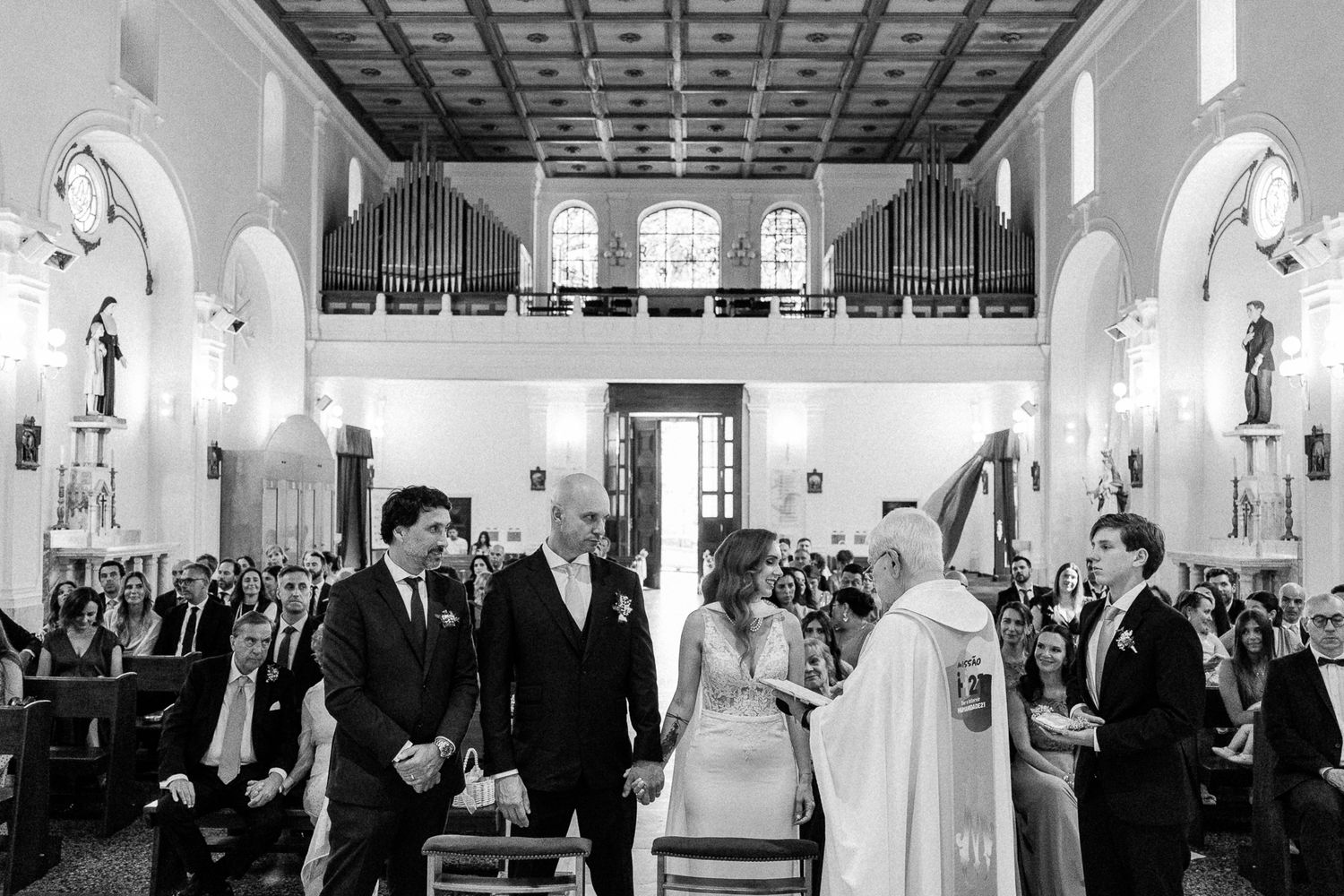 Black and white wedding ceremony photo inside an elegant church with guests seated in pews.
