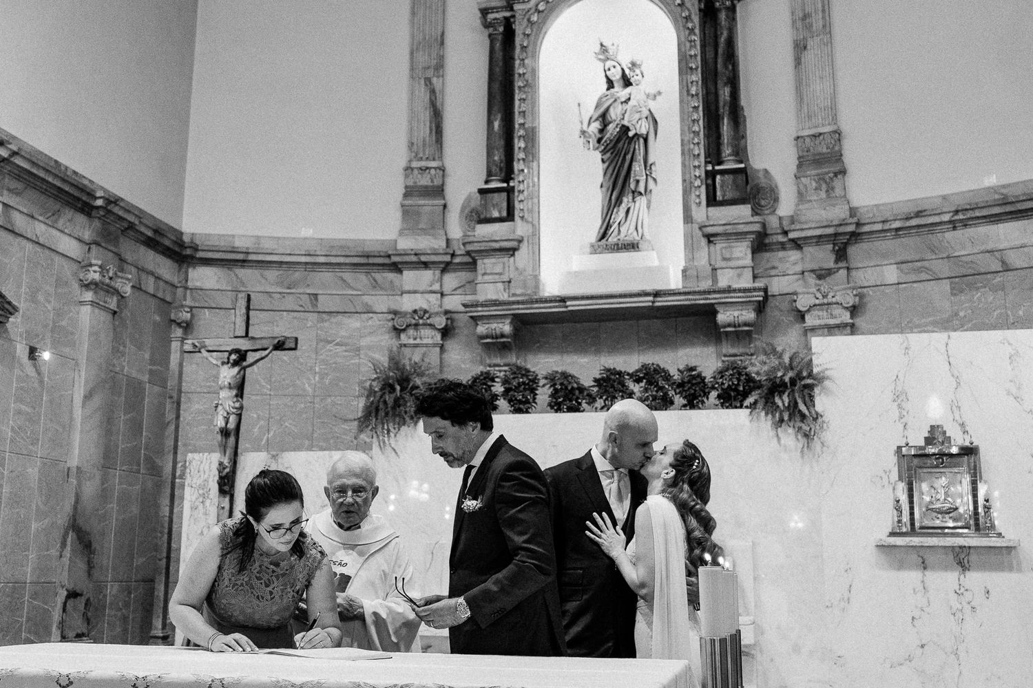 Black and white photo of a wedding ceremony at a church altar with a couple signing documents.