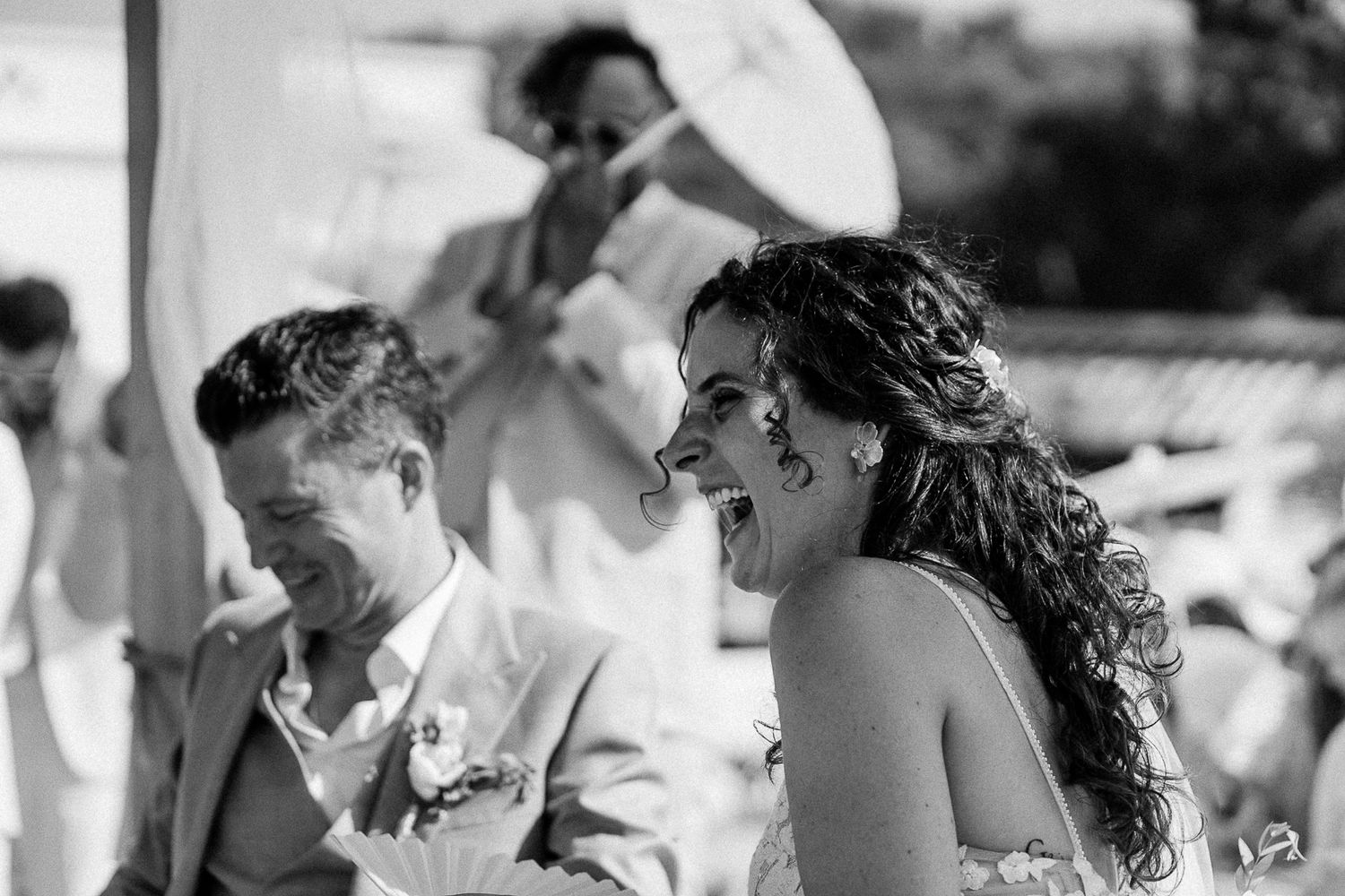 Black and white photo of a laughing bride and groom during an outdoor wedding ceremony.
