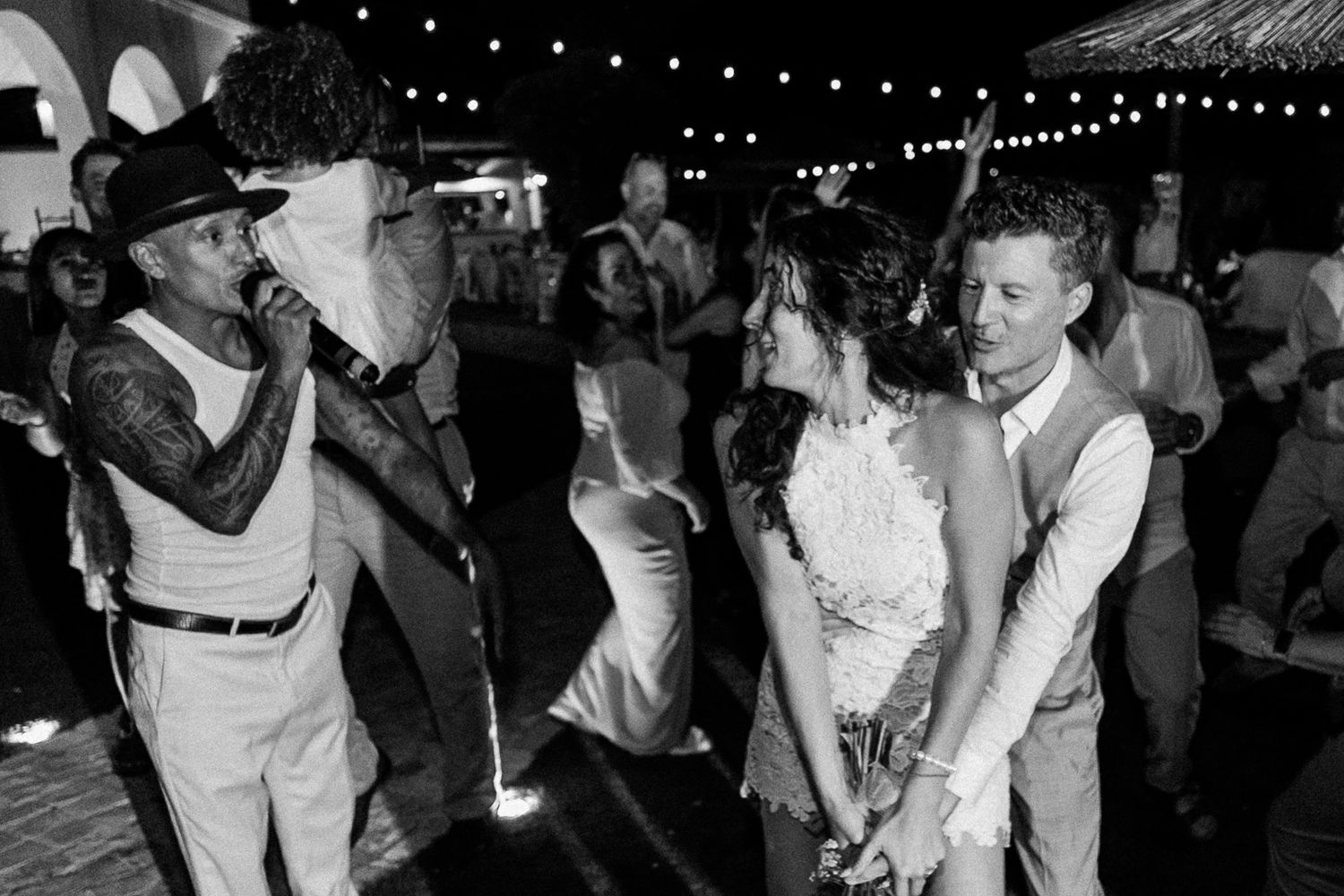 Black and white photo of a couple dancing at their wedding reception while a singer performs nearby.
