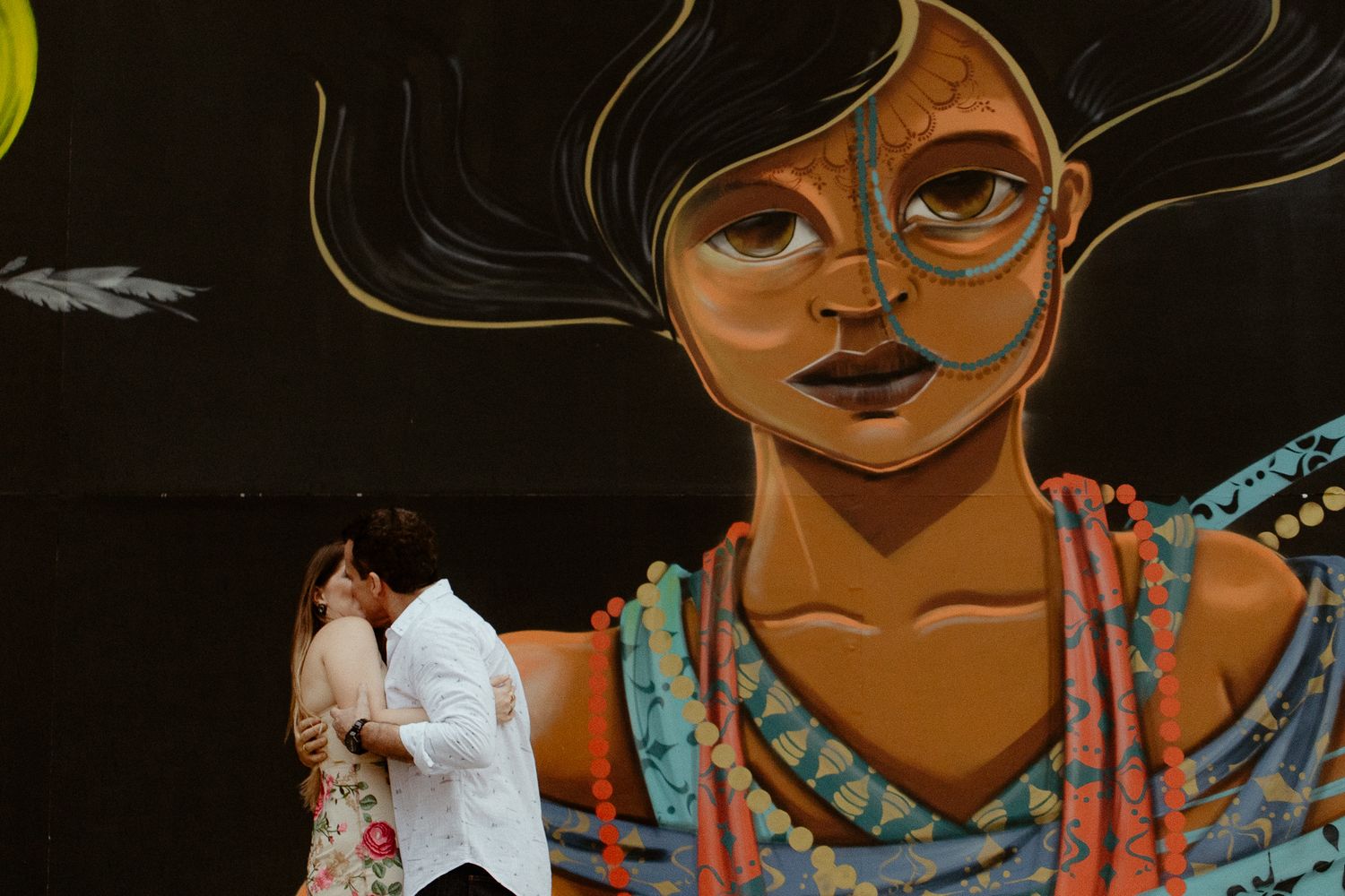 Street art mural of a woman in vibrant colors with turquoise and orange details against a dark background.