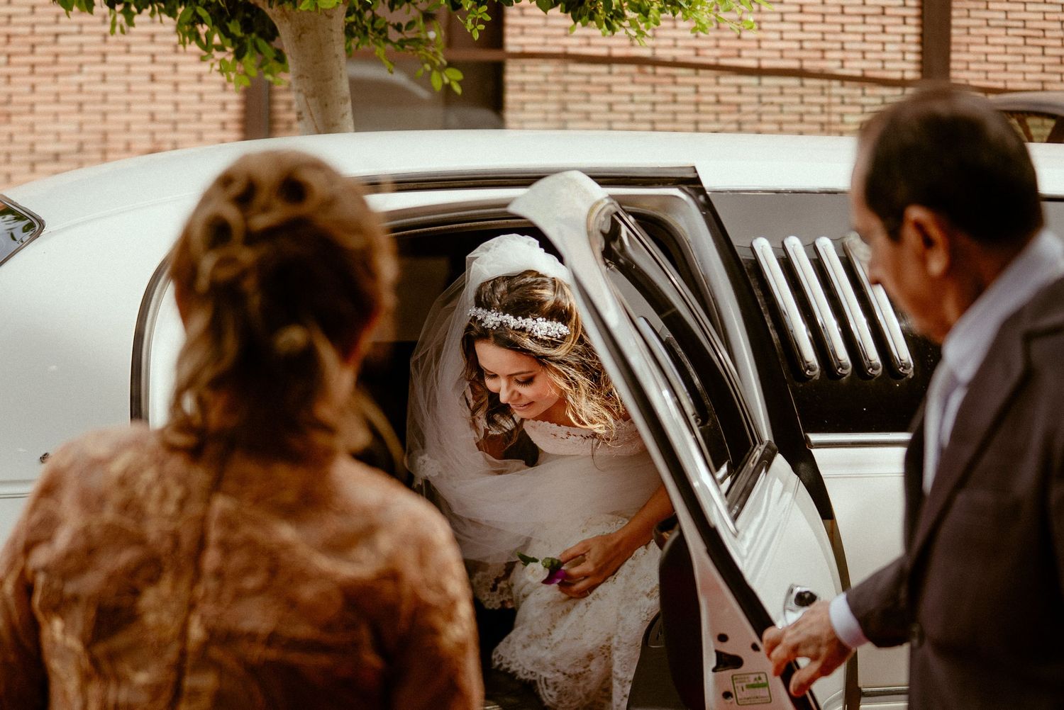 Wedding party walking outside a brick building to waiting cars parked along the curb.