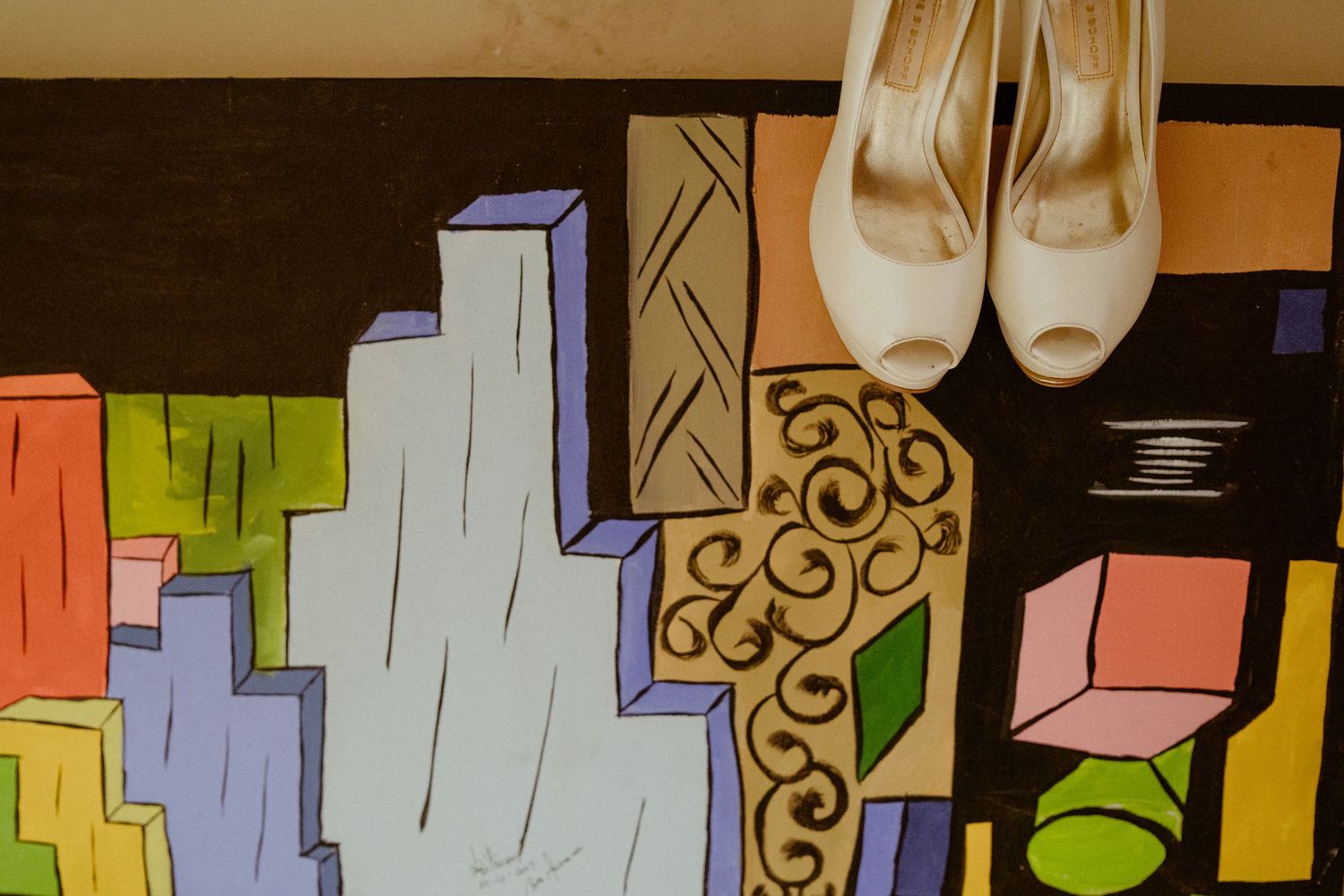 Abstract geometric wall art with colorful blocks and shapes displayed alongside white wedding shoes.