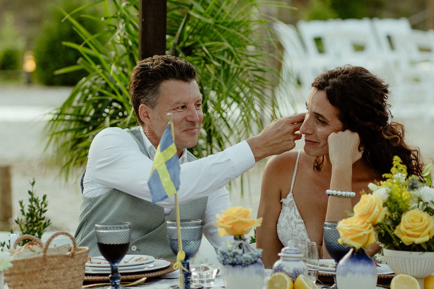 Bride and groom share a tender moment at their outdoor wedding reception table decorated with yellow roses.