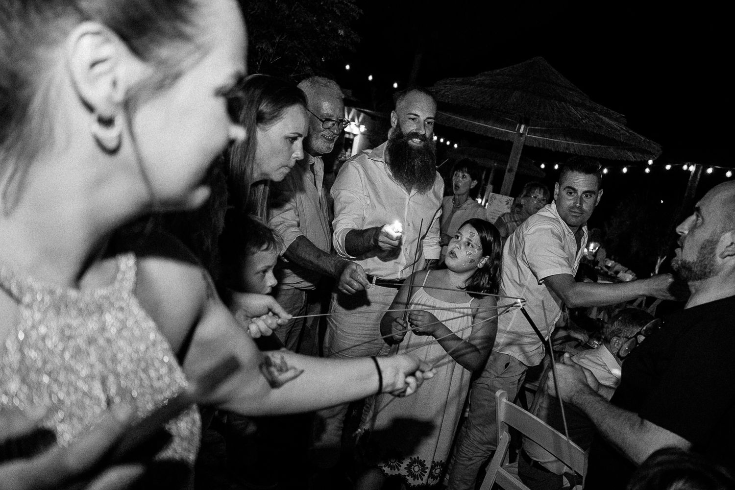 Black and white wedding reception photo of guests dancing and celebrating outdoors at night.