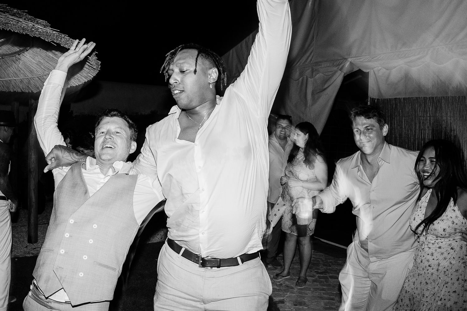 Black and white photo of guests dancing joyfully at a lively wedding reception party.