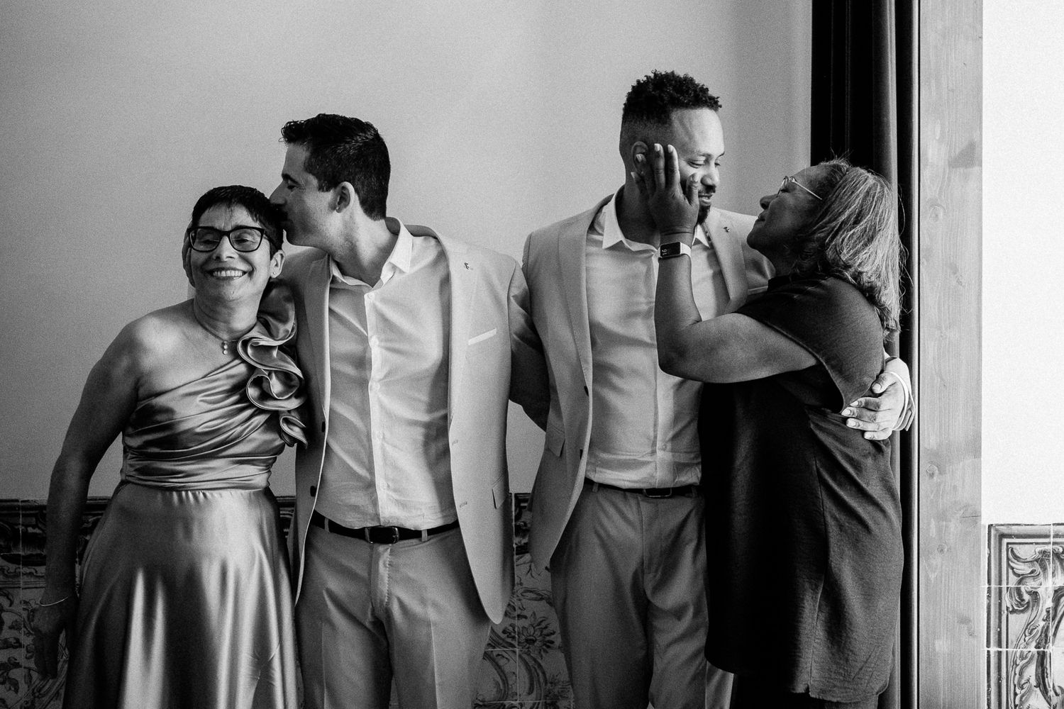 Black and white photo of two grooms laughing with family members at a joyful wedding celebration.