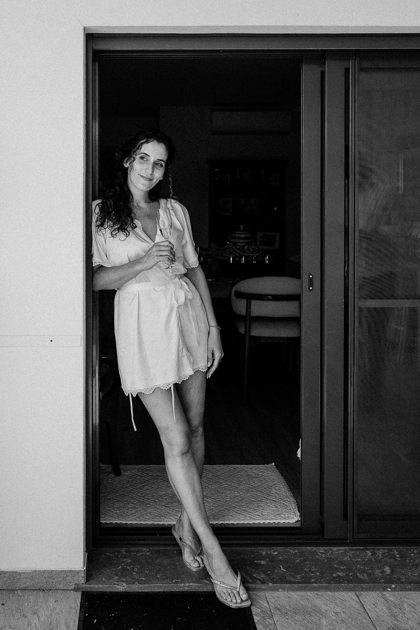 Black and white photo of a young woman in a short dress posing in a doorway with elegant long legs.