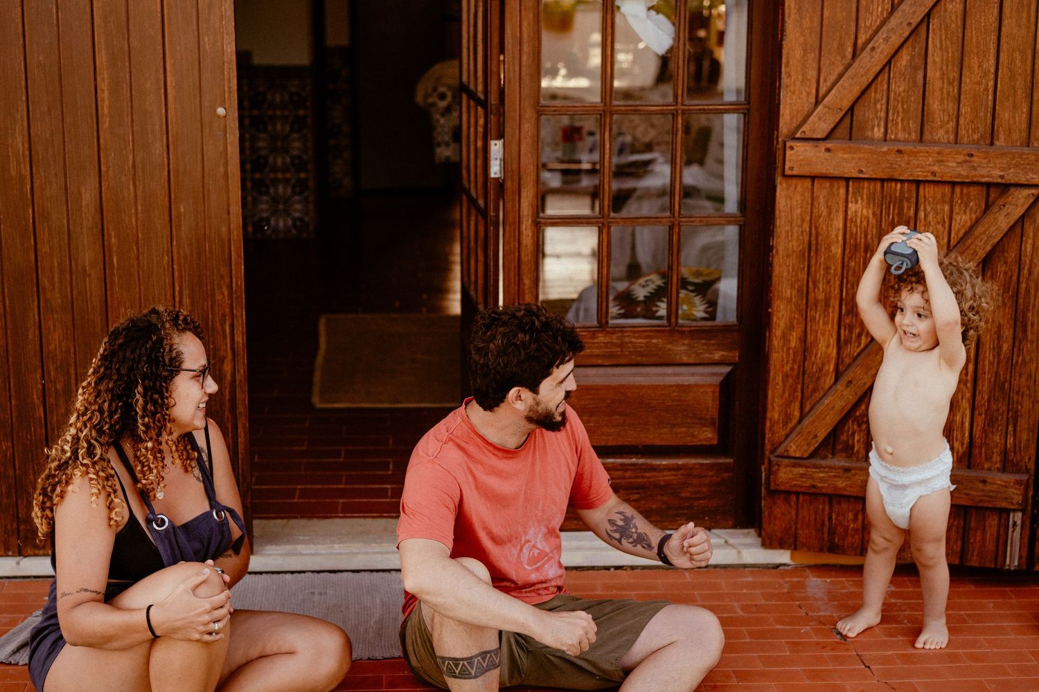 Several people relax and gather in a warm rustic wooden interior space with sunlight streaming in through windows.