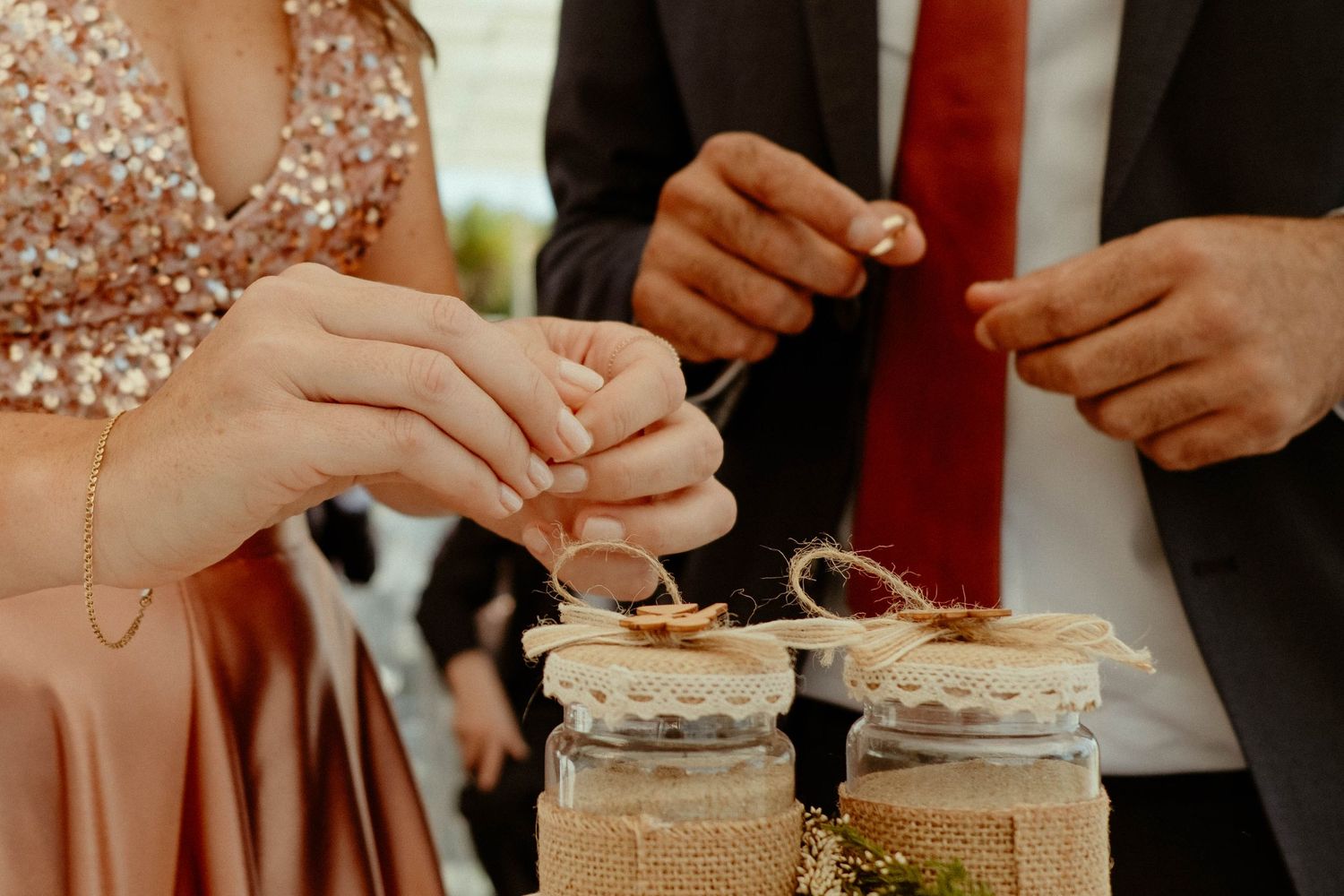 Hands decorating rustic mason jars with twine and lace for a vintage-style wedding reception centerpiece.