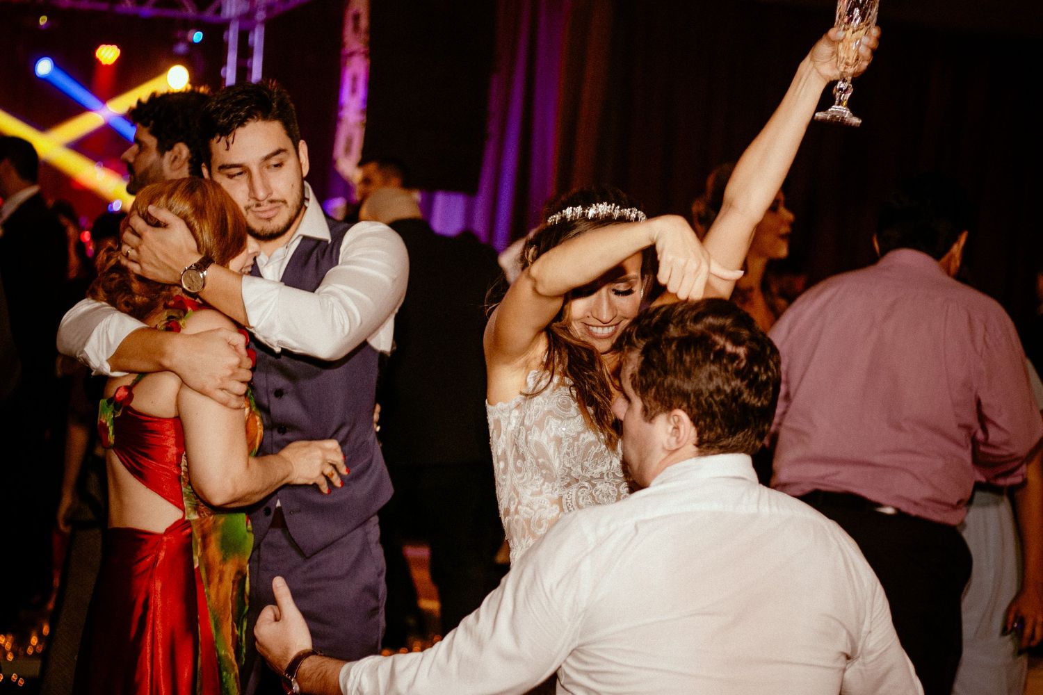 Wedding party members dance energetically under purple mood lighting during a reception celebration.