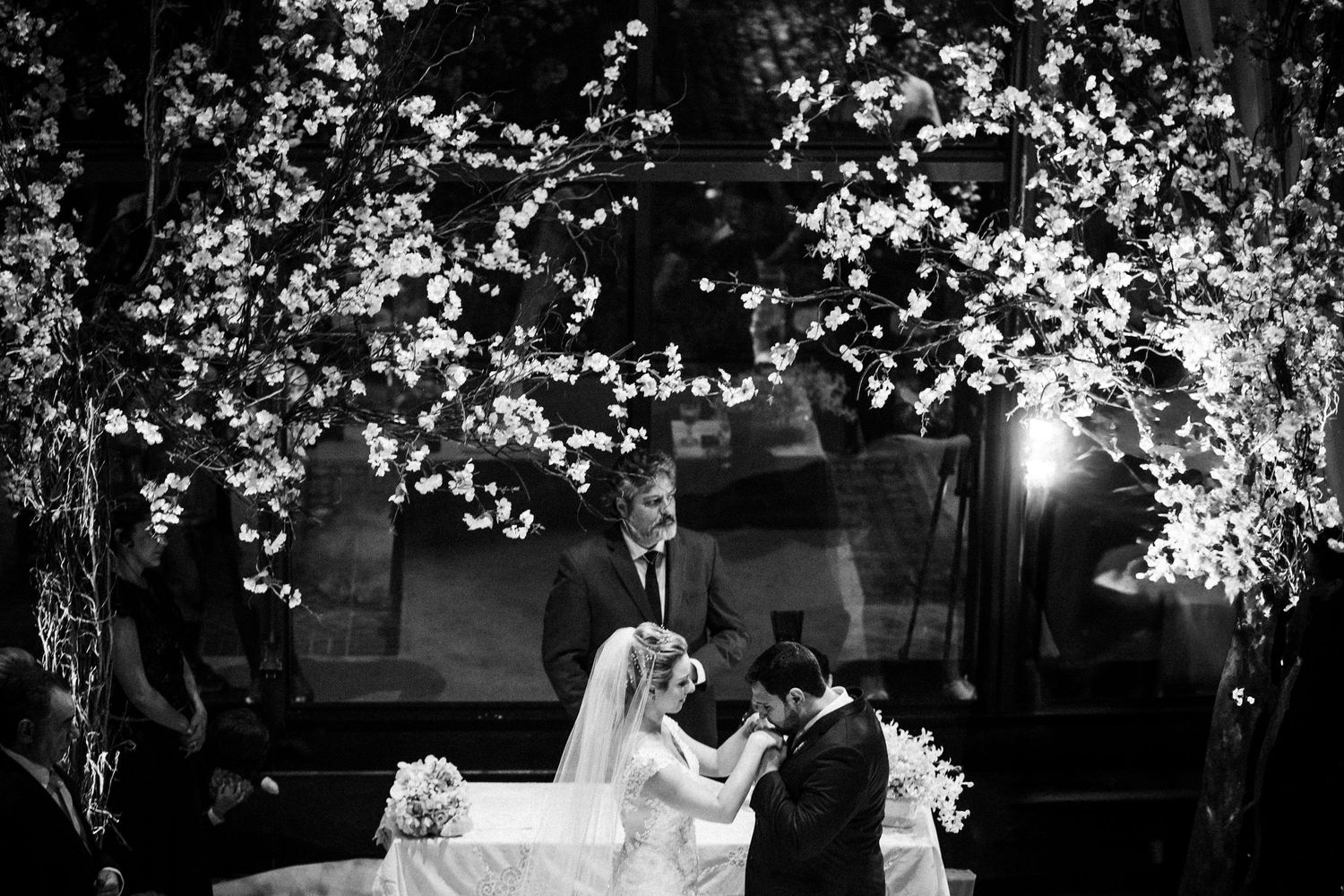 A dramatic black and white wedding ceremony scene with illuminated cherry blossom trees.
