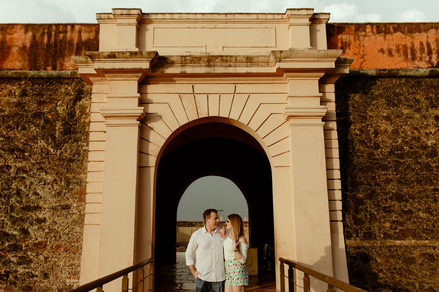 Romantic couple embraces under an elegant white archway during golden hour at a historic estate.