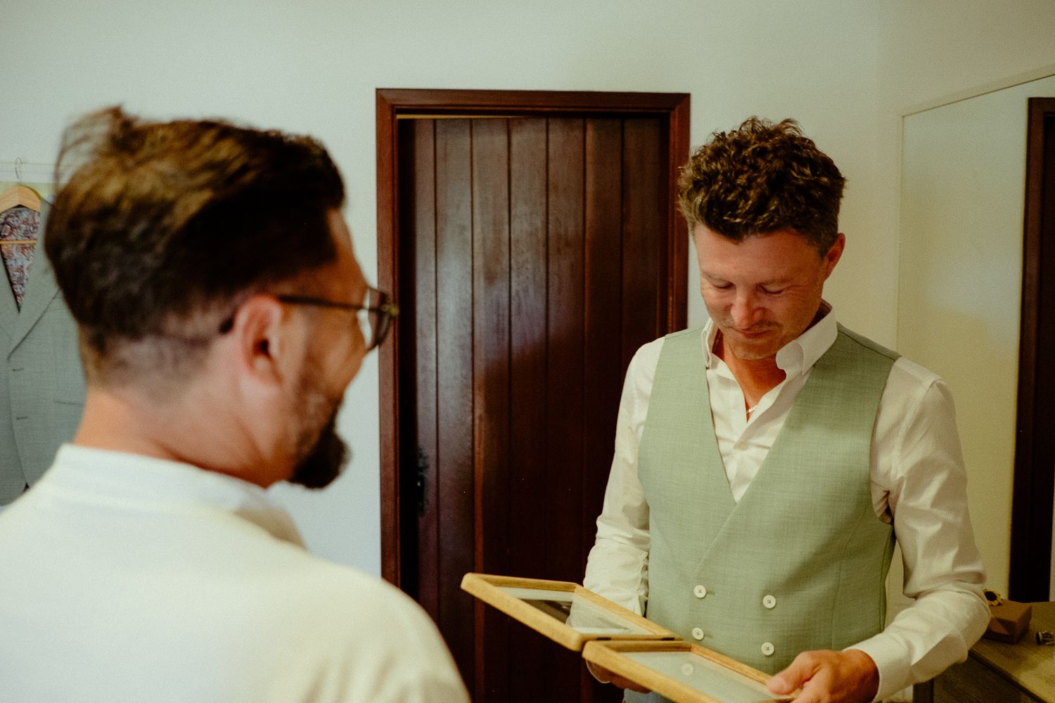 Two men in formal attire examine a wooden frame indoors, ideal for wedding preparation photography.