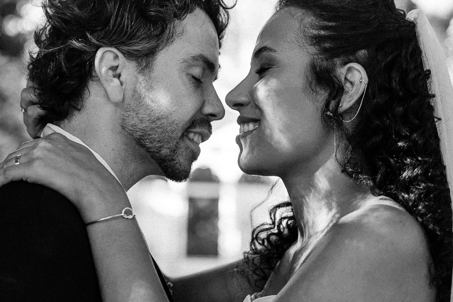 Black and white photo of a romantic couple sharing an intimate moment, smiling closely at each other at a wedding.