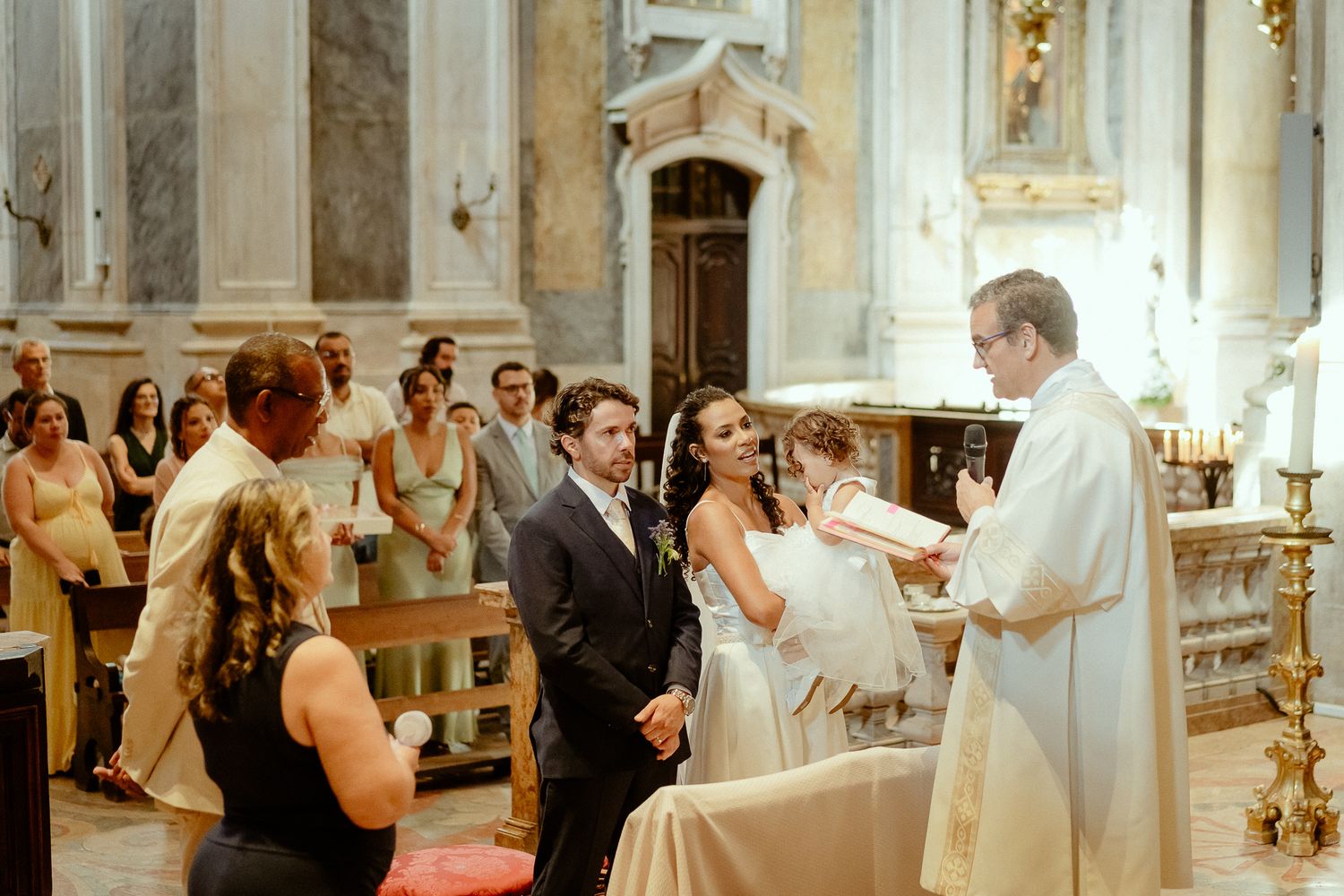 Bride and groom exchanging vows with a priest in an elegant marble church during a traditional wedding ceremony.