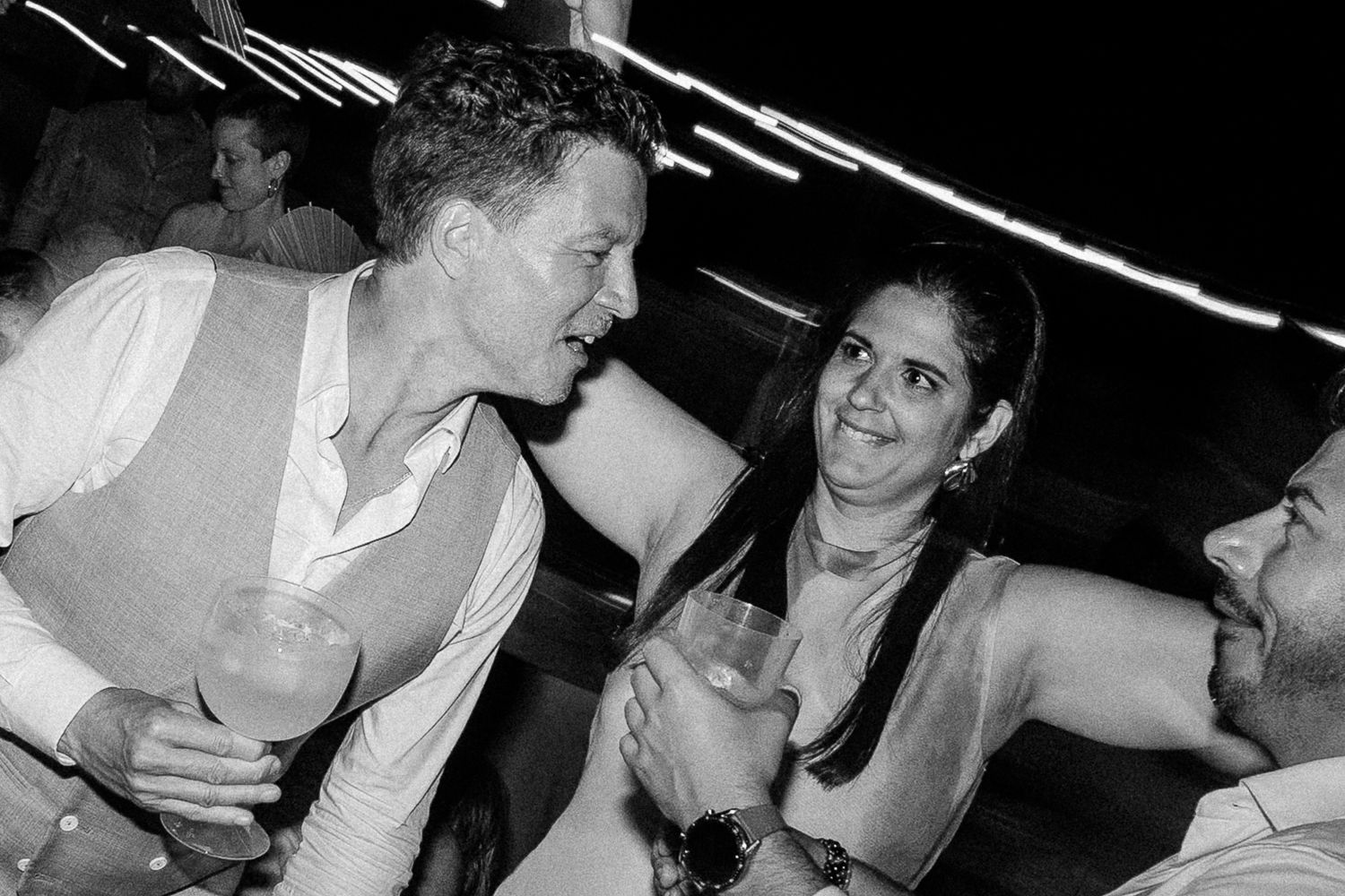 Black and white photo of people socializing at a party, smiling and holding drinks in a lively nighttime setting.