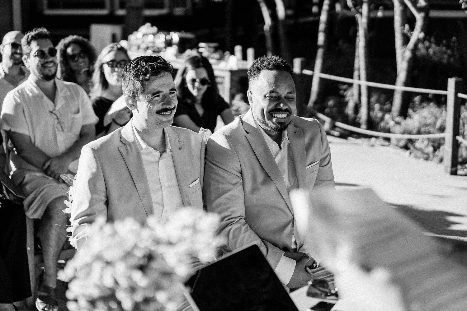Two grooms share a joyful moment at their outdoor wedding ceremony in black and white photo.