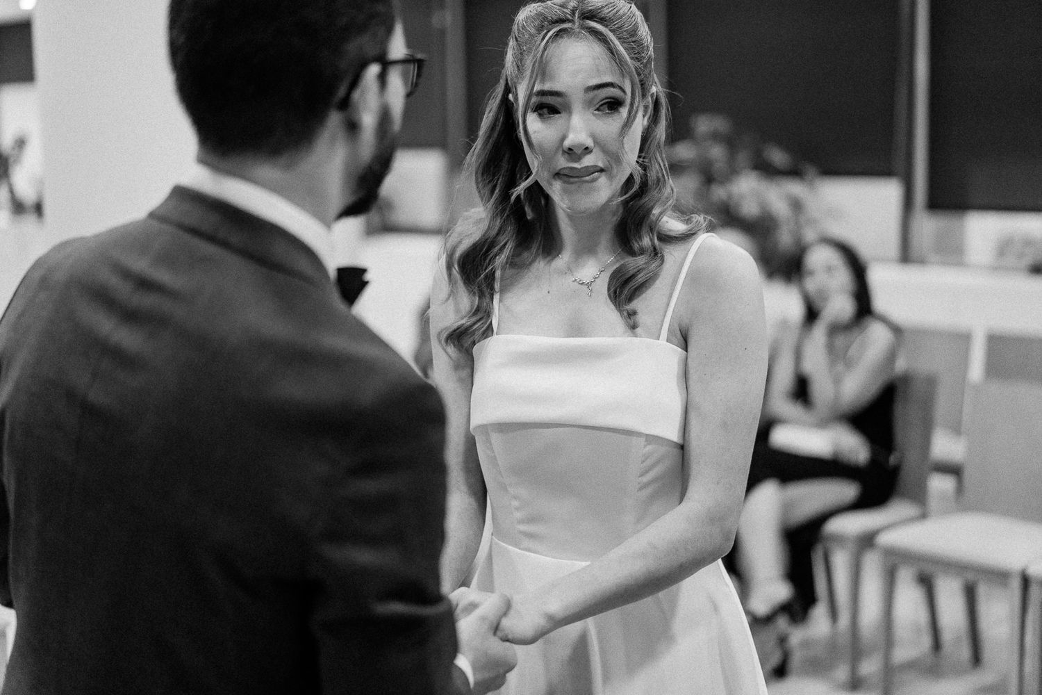 Black and white photo of a bride in a white dress holding hands with groom during an emotional wedding ceremony.