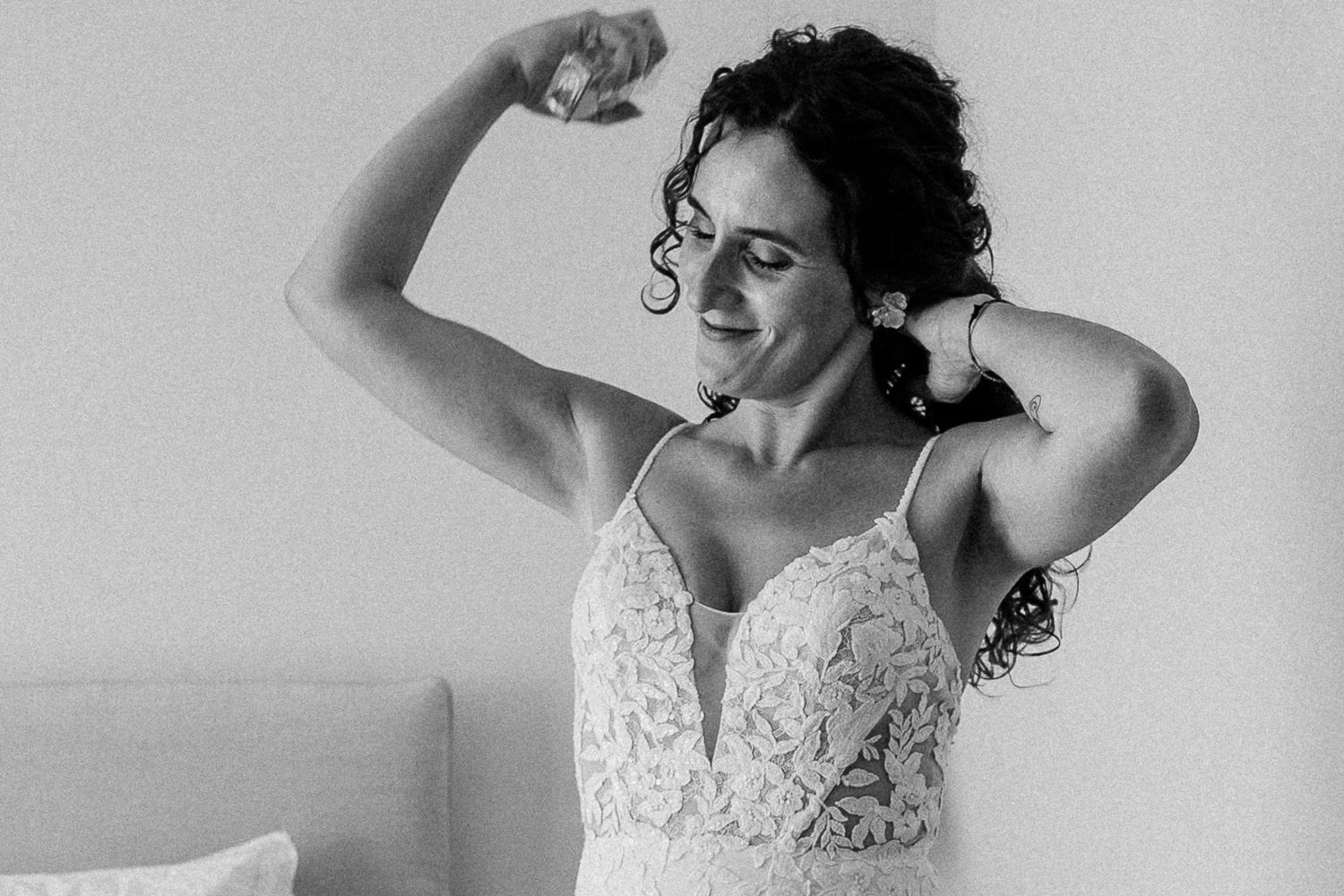 Bride in lace wedding dress flexing her arm muscle, smiling confidently in a black and white photo.