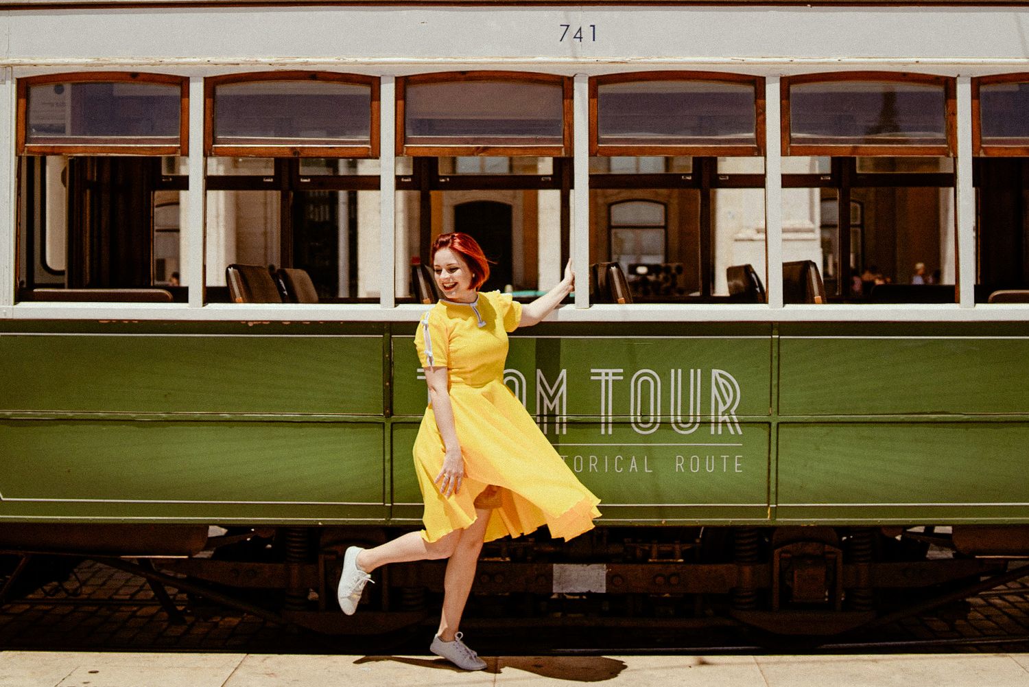 A playful dance pose next to a vintage green tram car with 'M TOUR' signage.
