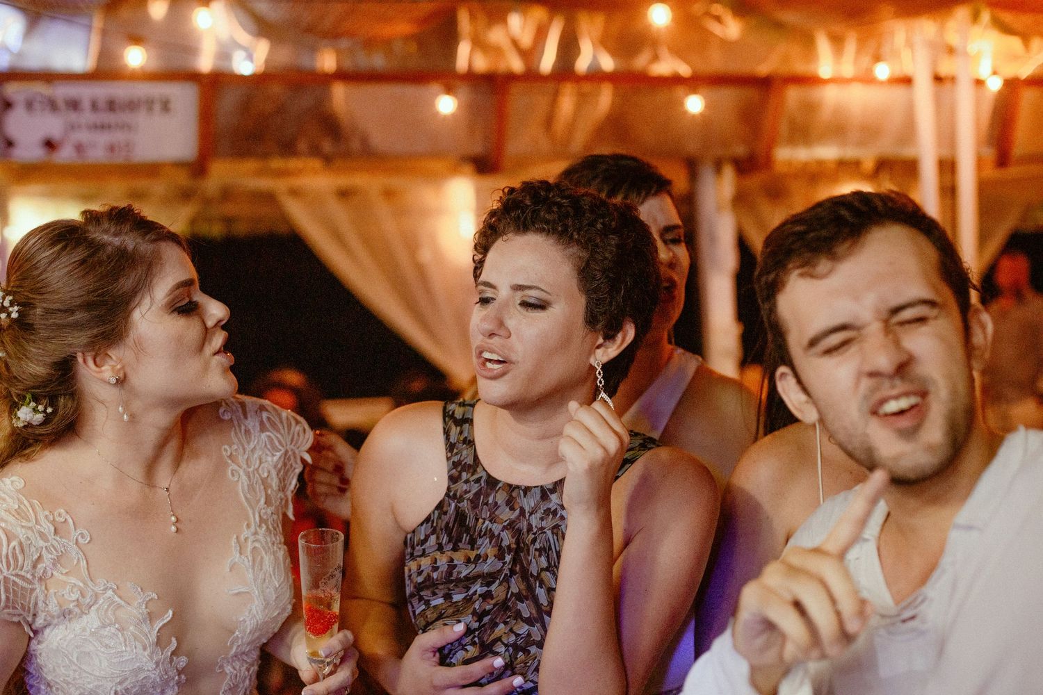 A group dances exuberantly at a reception or party in a warmly lit indoor venue.
