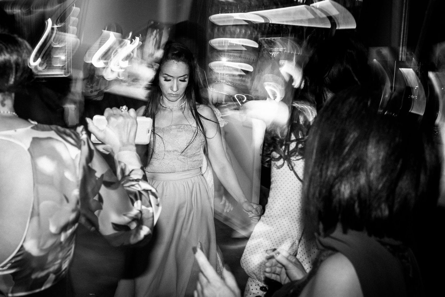 Group of wedding guests dancing and celebrating on a nightclub dance floor under dim lighting.