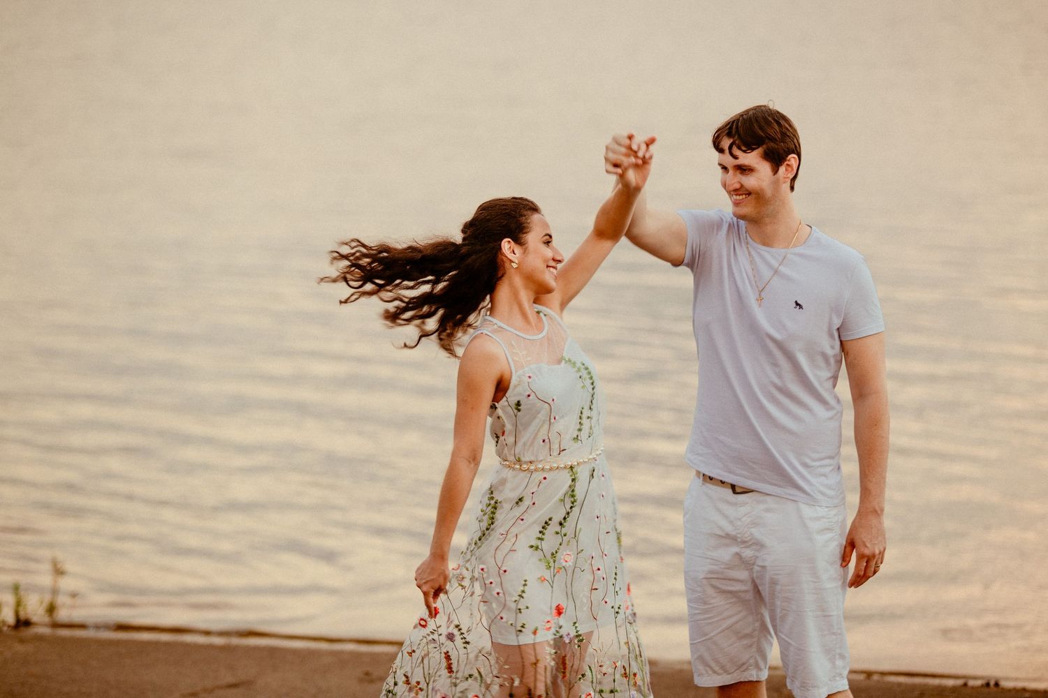 A couple dances and twirls together on a peaceful beach during sunset, creating a joyful romantic moment.