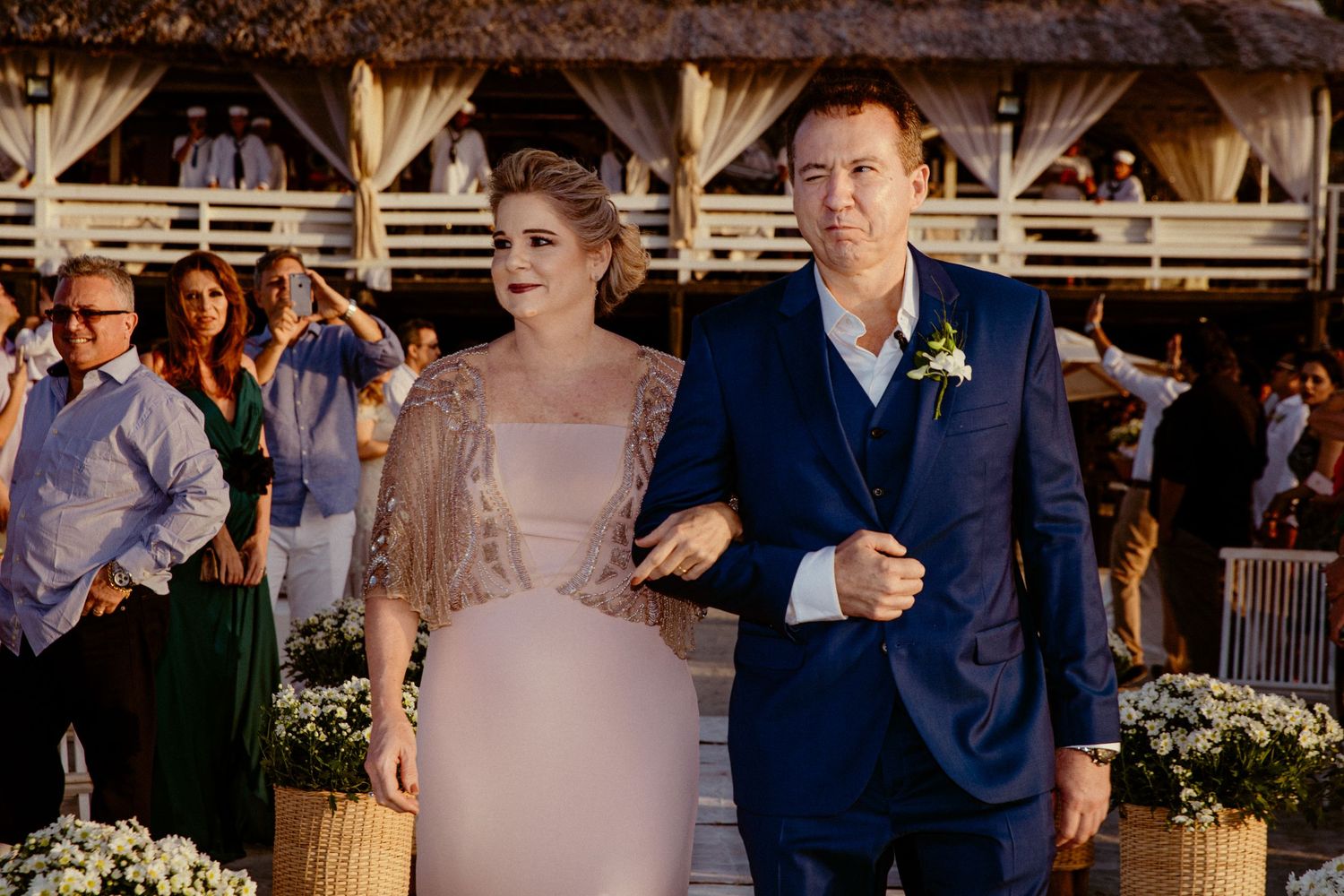 Couple at rustic outdoor wedding venue with wooden beams and floral decorations.
