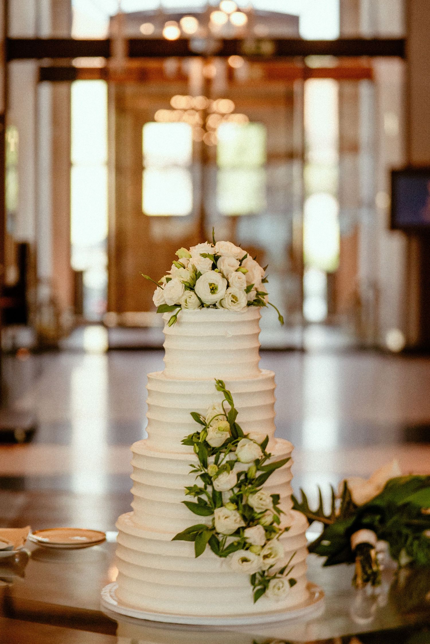 Elegant white wedding cake decorated with fresh flowers and greenery in natural light.
