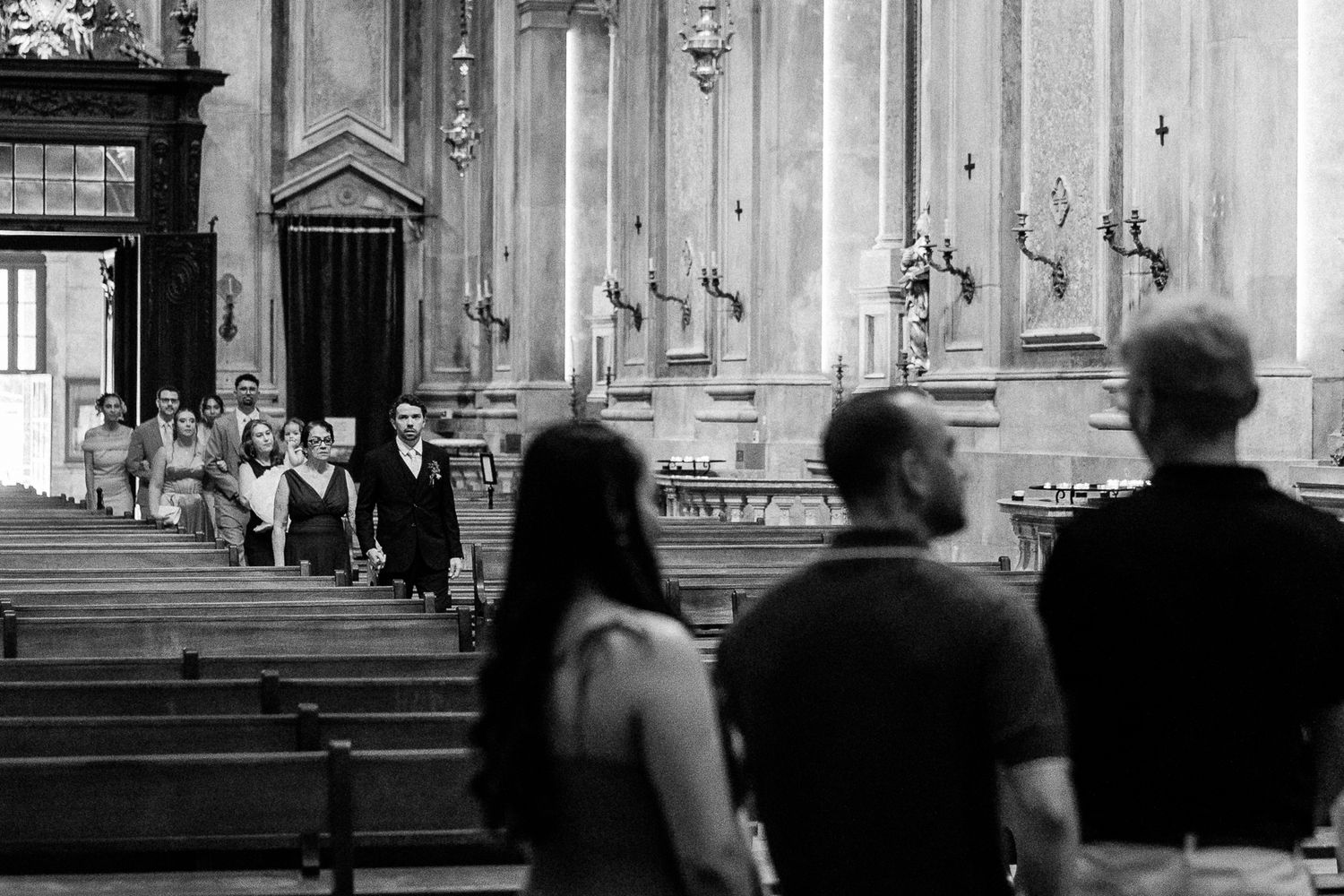 Black and white photo of a wedding procession inside an ornate church with guests seated in pews.