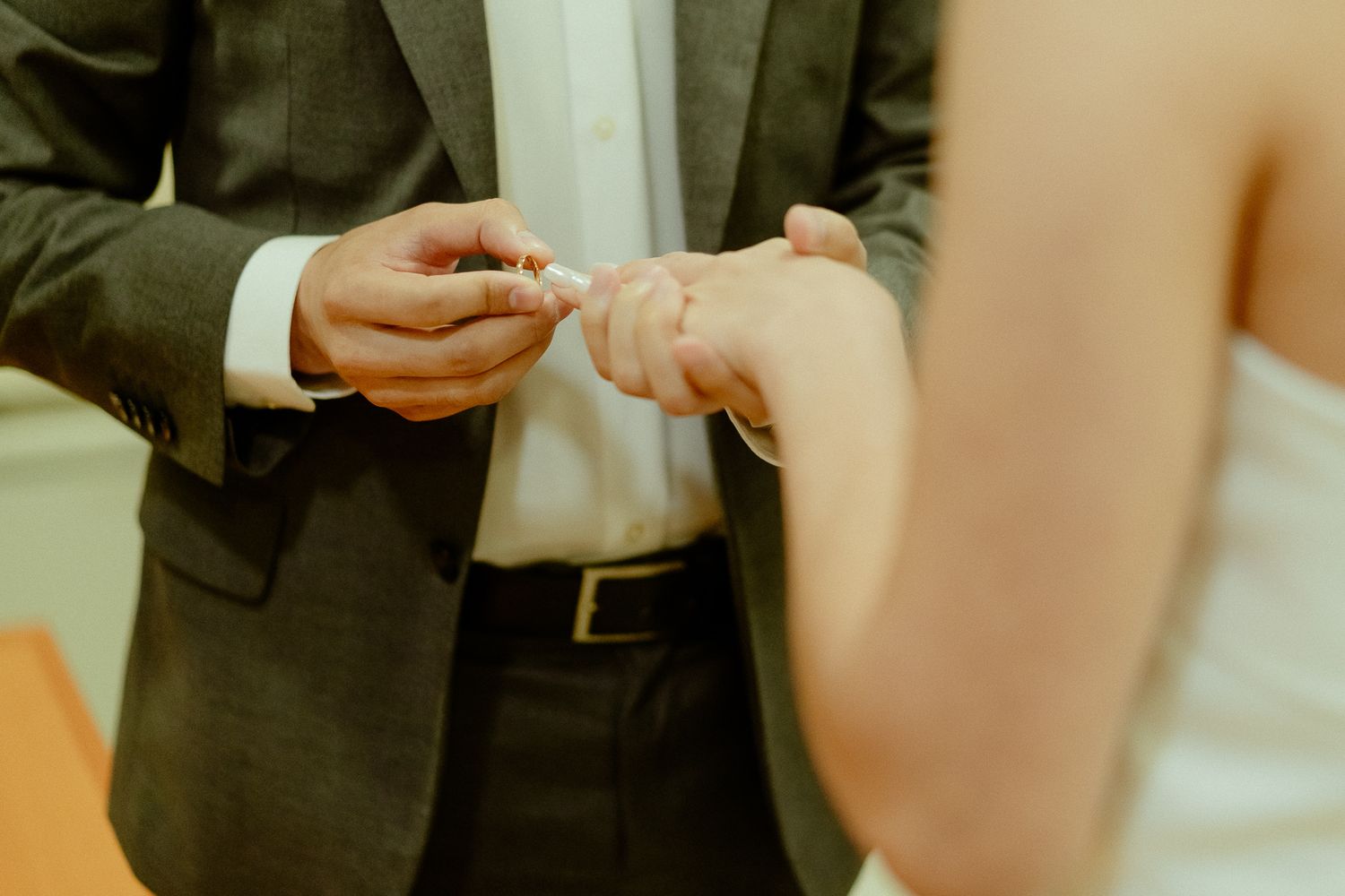 Groom placing a wedding ring on bride's finger during ceremony, close-up of hands in elegant attire.