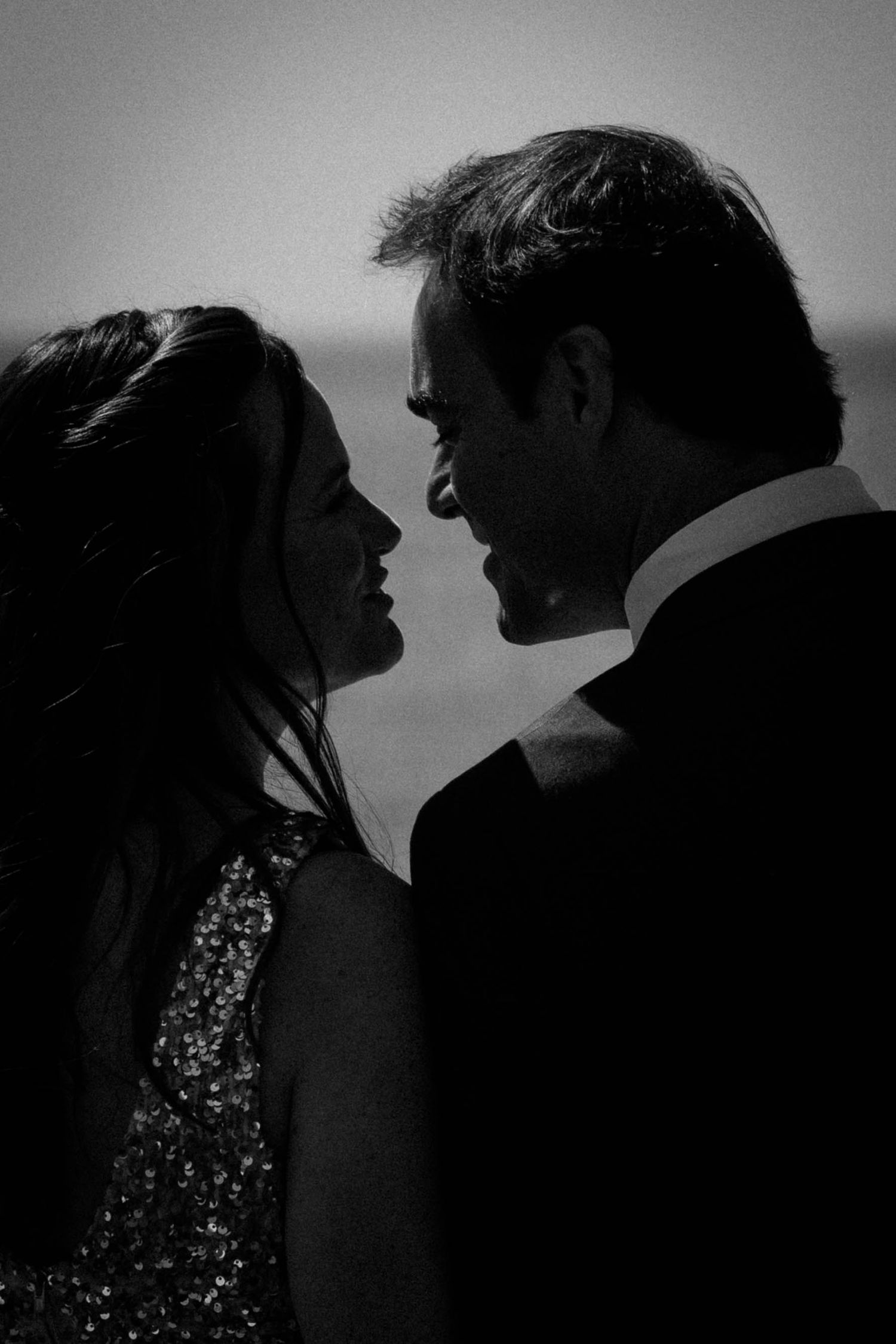 A romantic black and white silhouette of a couple in formal wear gazing at each other against a soft background.