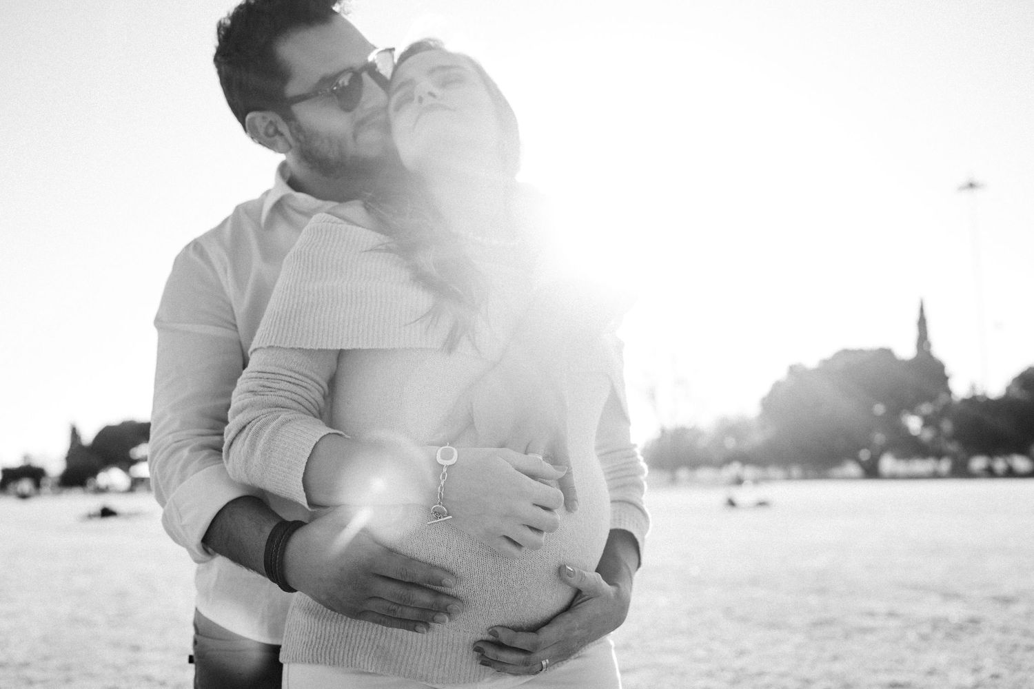 Black and white photo of a tender embrace outdoors with sunlight creating a dreamy lens flare effect.