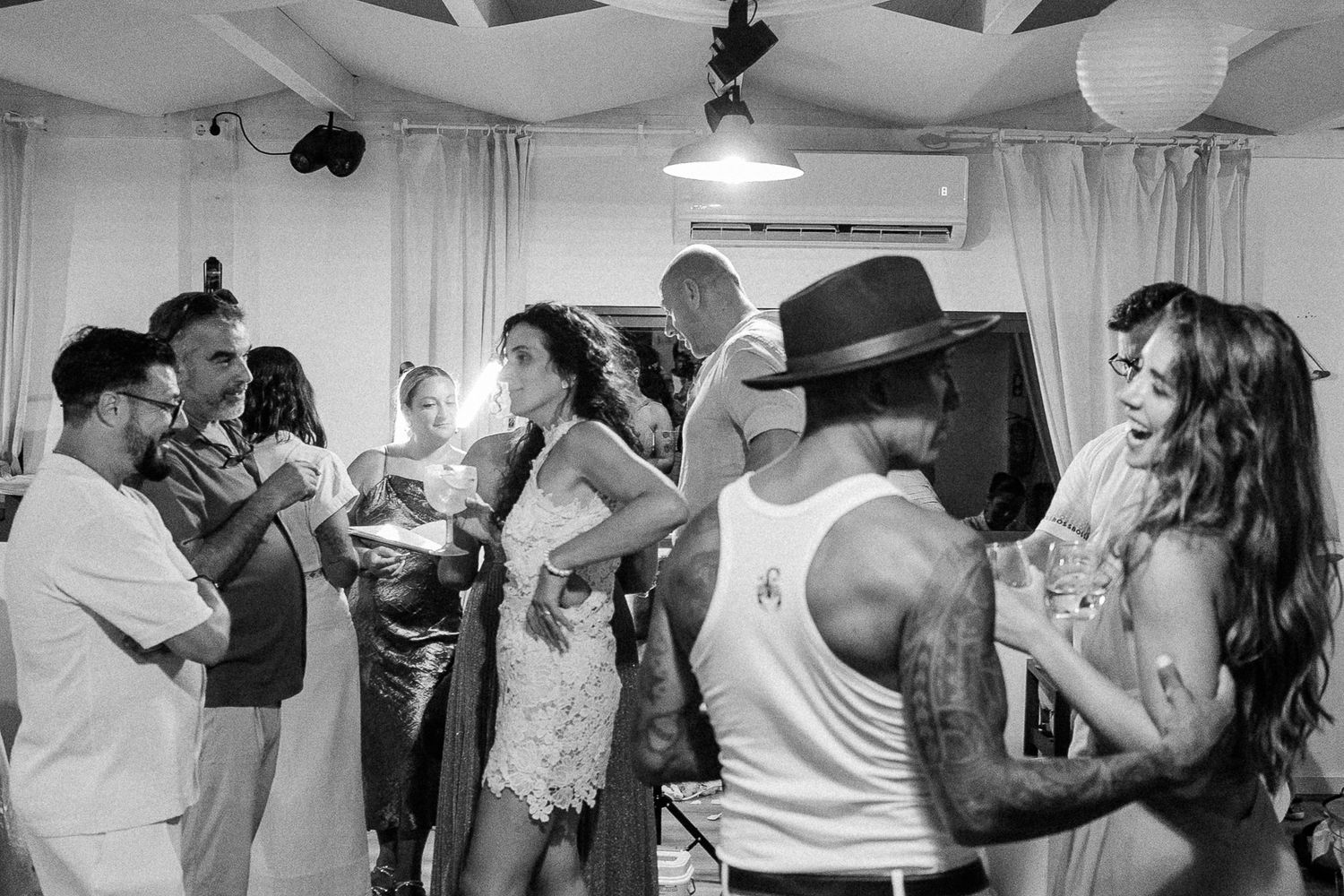 Black and white photo of guests dancing and socializing at a lively indoor party or wedding reception.
