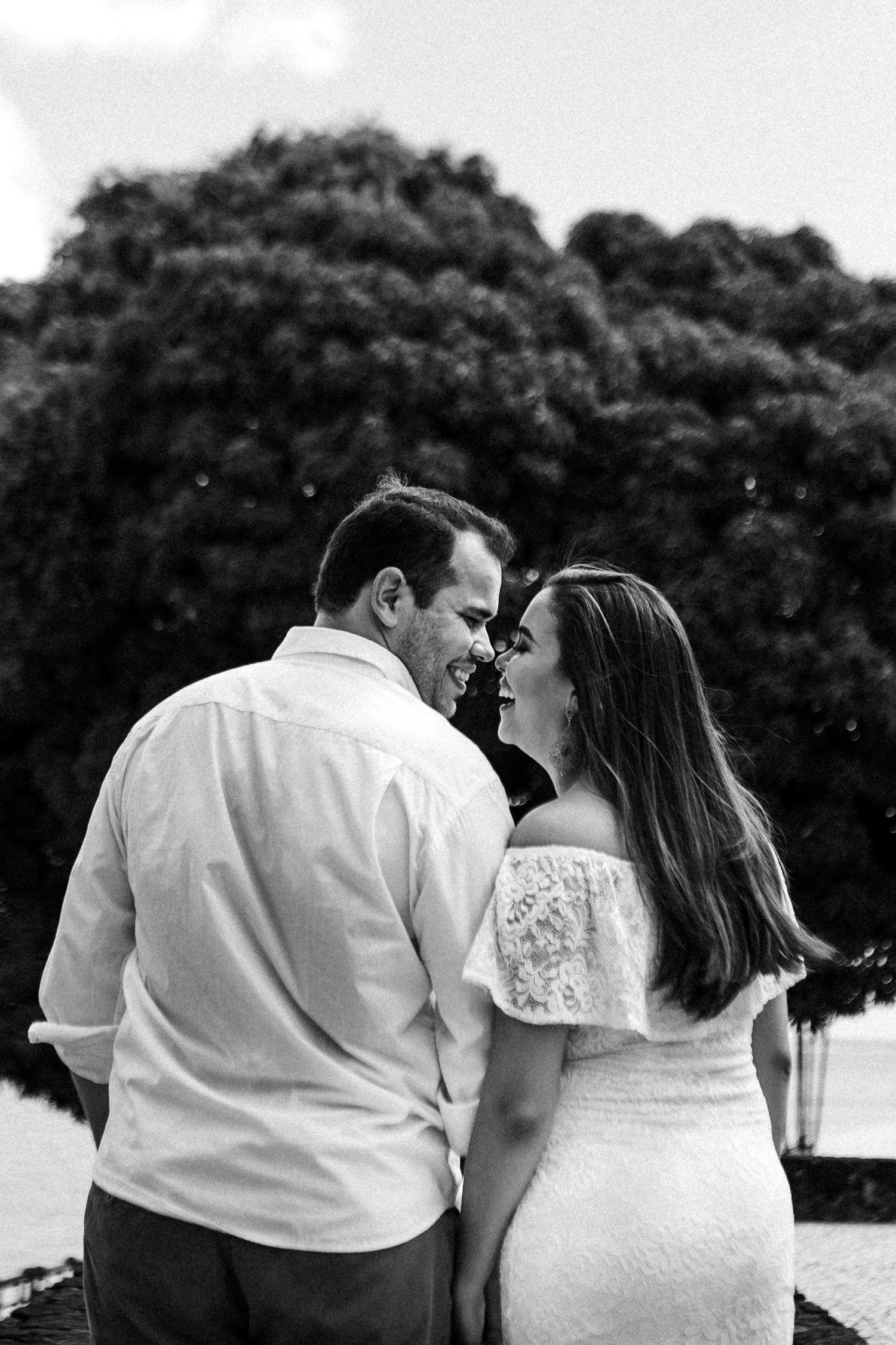 Romantic black and white photo of a couple sharing an intimate moment outdoors against leafy trees.