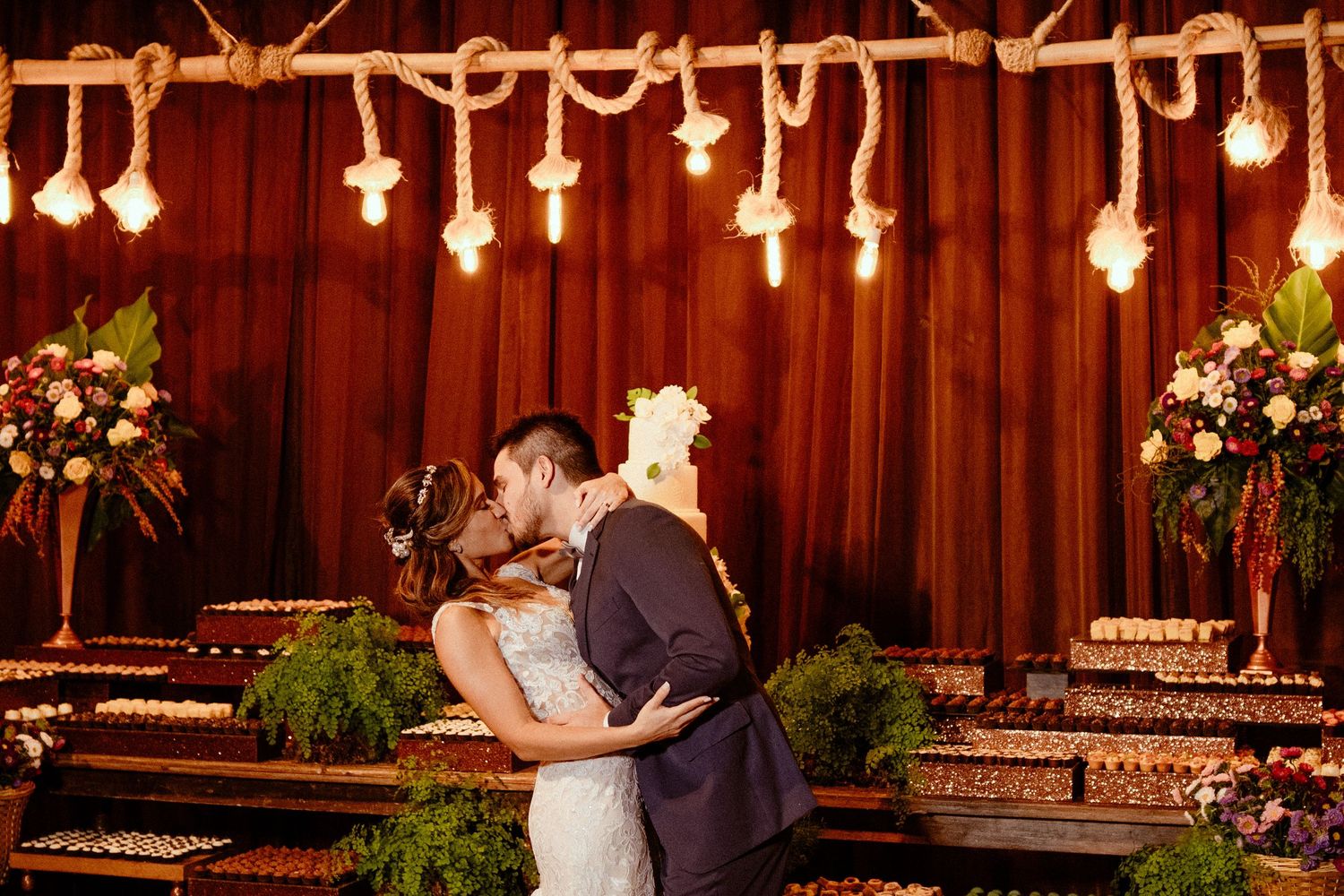 A romantic barn wedding ceremony with warm lighting from hanging Edison bulbs and rustic wooden walls.