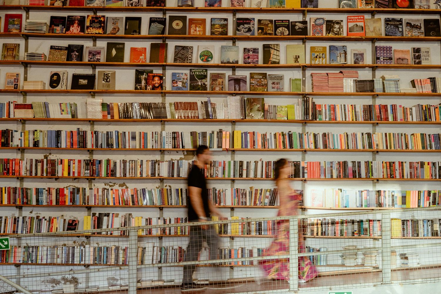 Seven connected photos show extensive library bookshelves arranged in horizontal rows filled with colorful books and media.