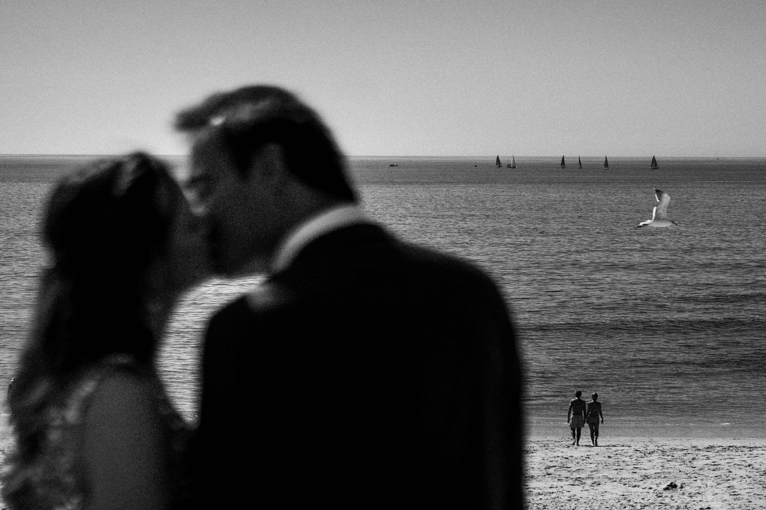 Silhouetted figures walk along a beach at sunset with ocean waves in the background.
