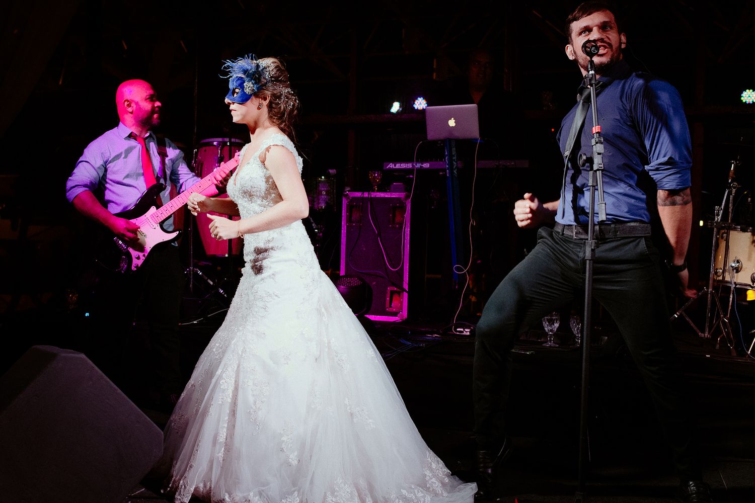 A couple dances together at a wedding reception with musicians performing on stage in the background.