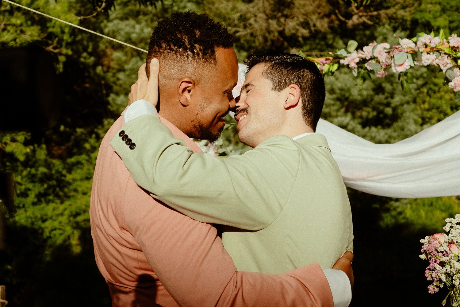Two grooms embracing and sharing a romantic moment at their outdoor wedding ceremony.