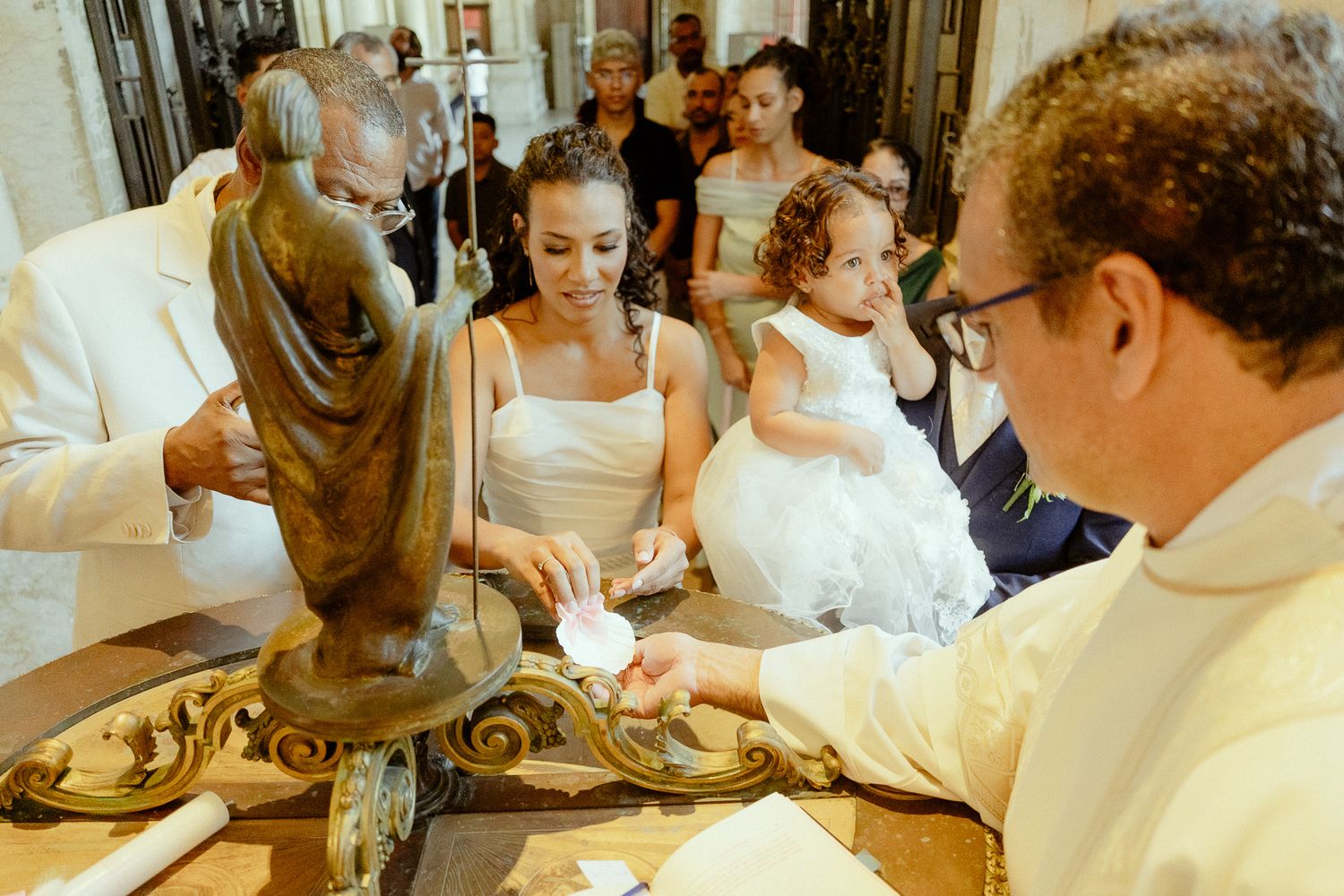 Priest performs baptism ceremony with woman and child at ornate church font.