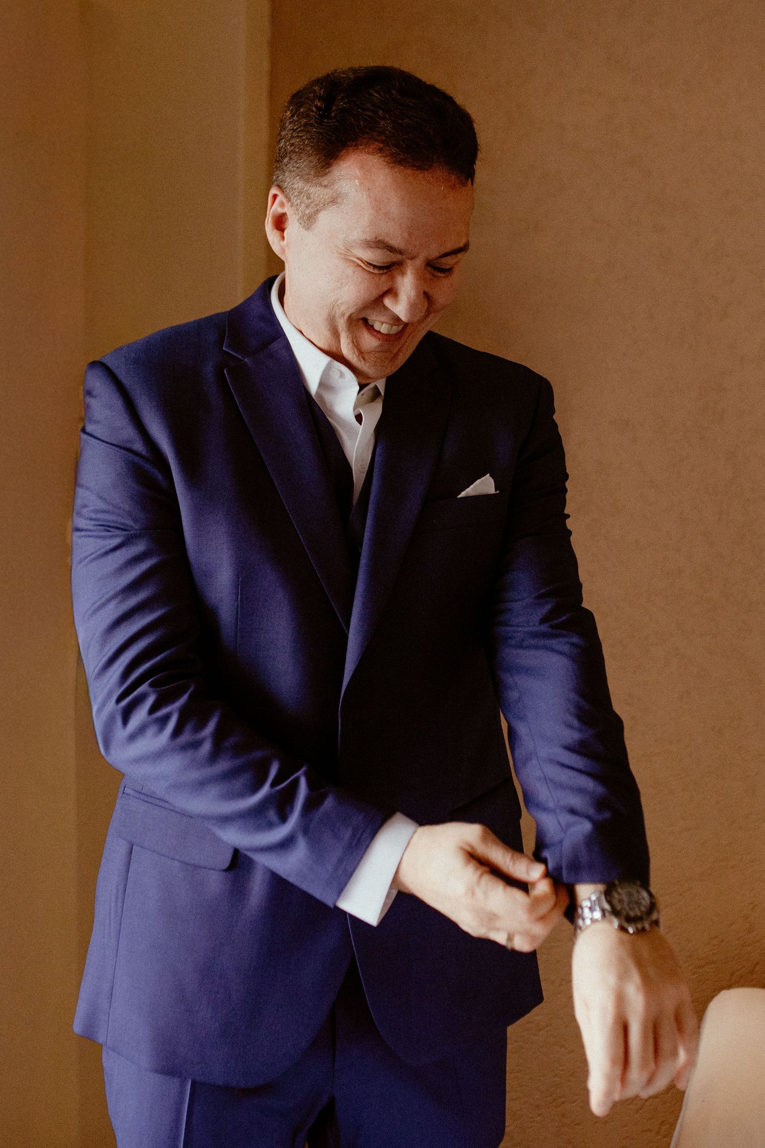 Person in navy blue suit laughs and gestures expressively in a series of candid poses against brown background.