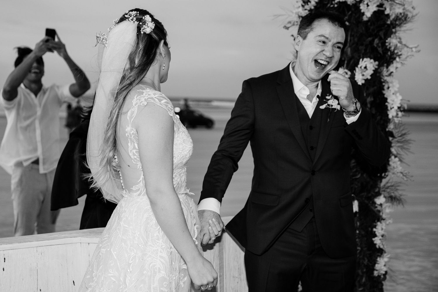 A joyful wedding couple share a candid moment together on a beach during their black and white wedding ceremony.