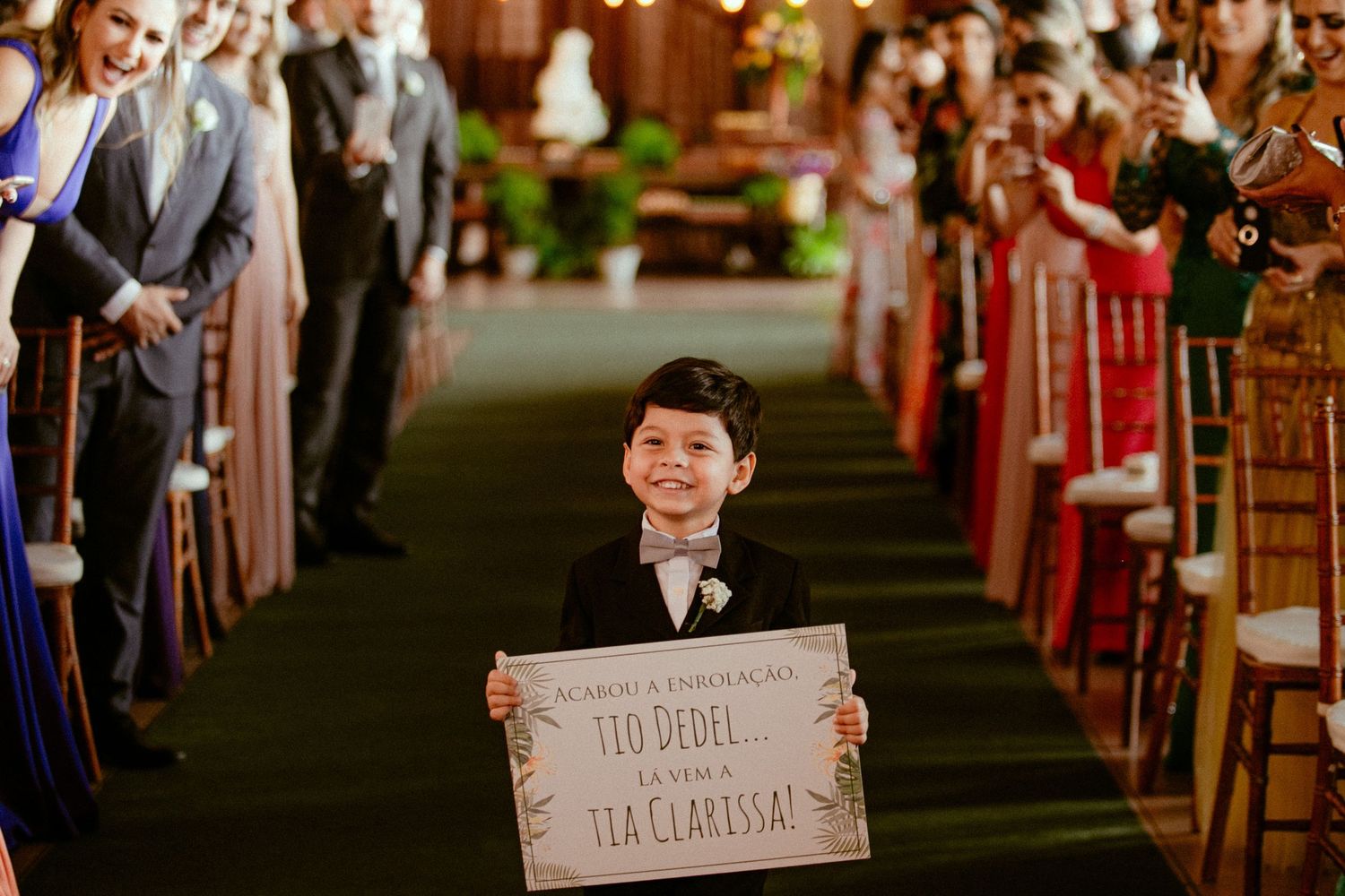Young attendant walks down church aisle holding decorative wedding sign during ceremony.