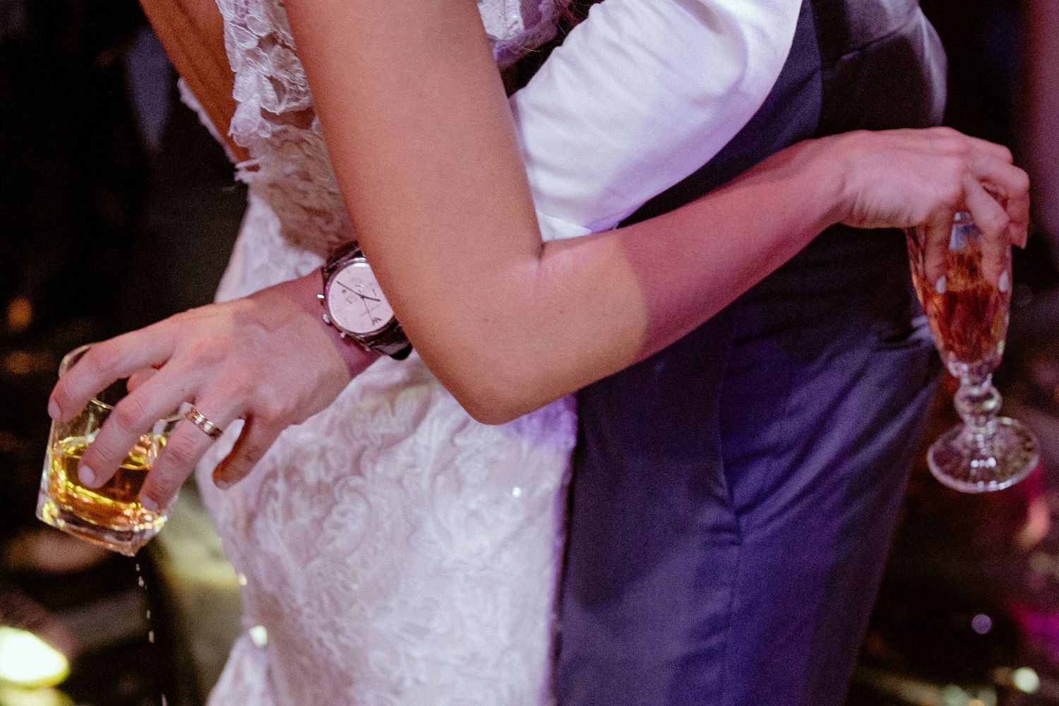 Wedding couple slow dances together holding champagne glasses at romantic evening reception.