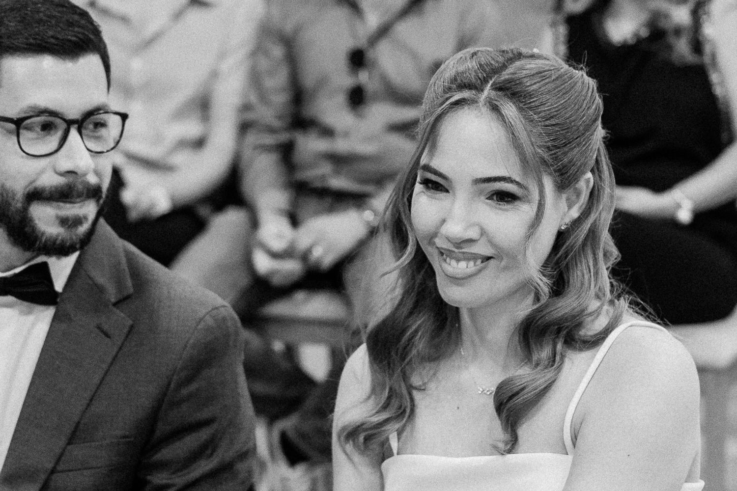 Black and white wedding photo of a smiling bride in a strapless gown seated beside a bearded groom in a suit.