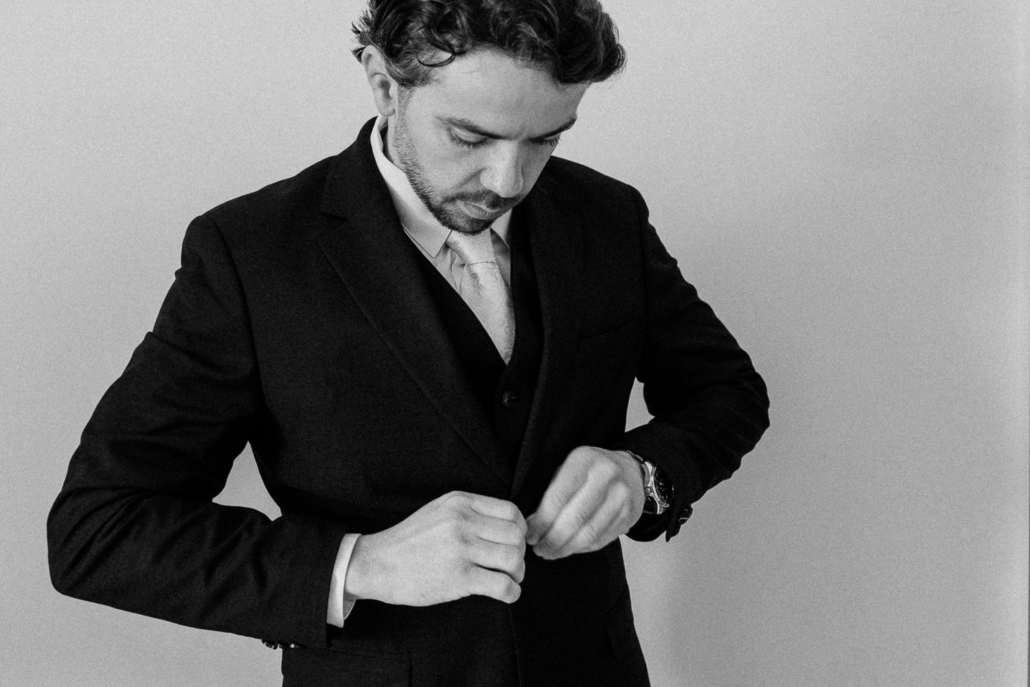 Groom in black suit buttoning jacket in black and white wedding preparation photo.