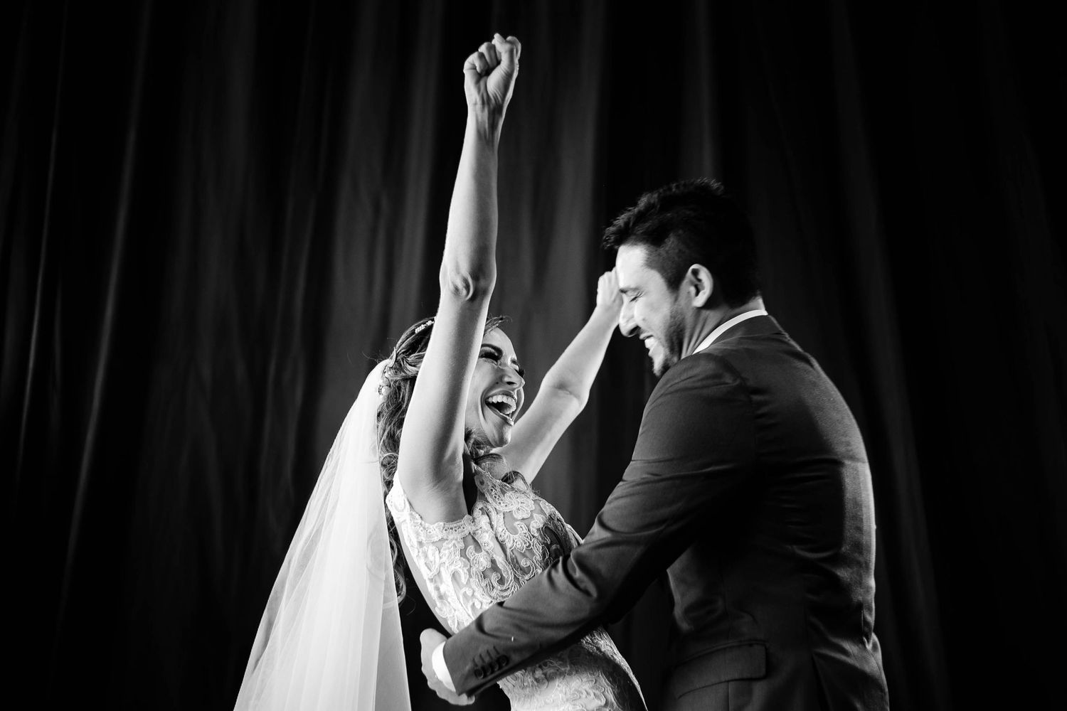 A black and white photo captures a joyful moment of a bride and groom dancing together at their wedding reception.